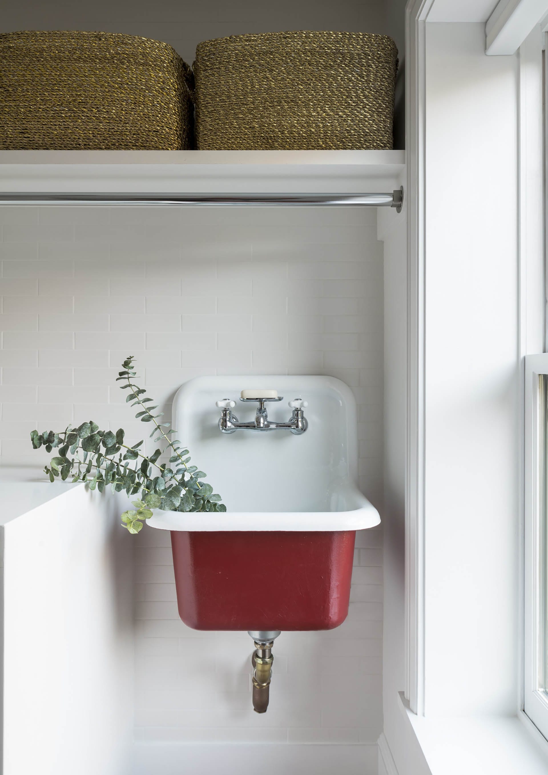 Red sink in a laundry room with white subway tiles on the wall.