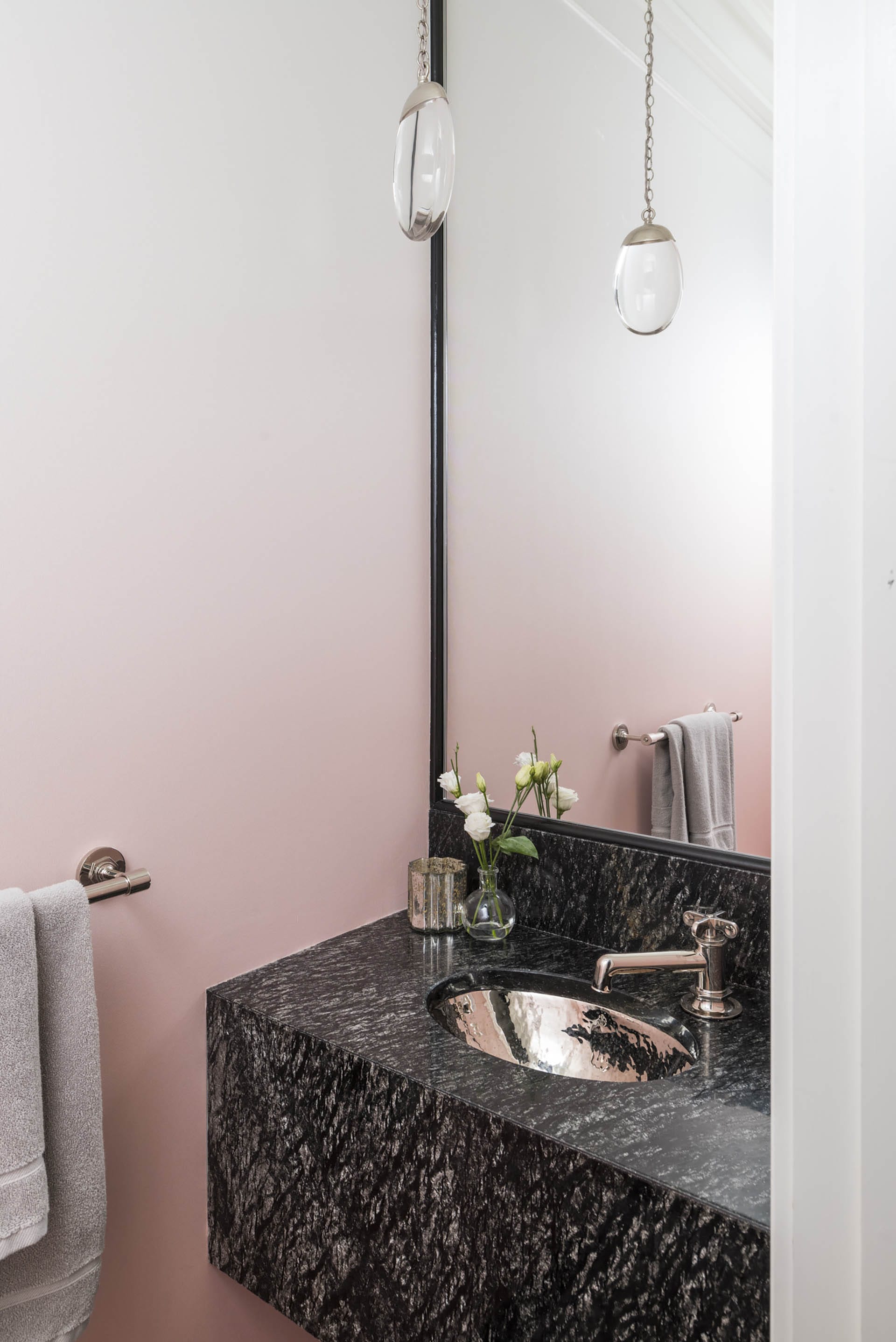 Powder room with white and pink ombre wallpaper, a dark stone vanity, and a single hanging pendant light