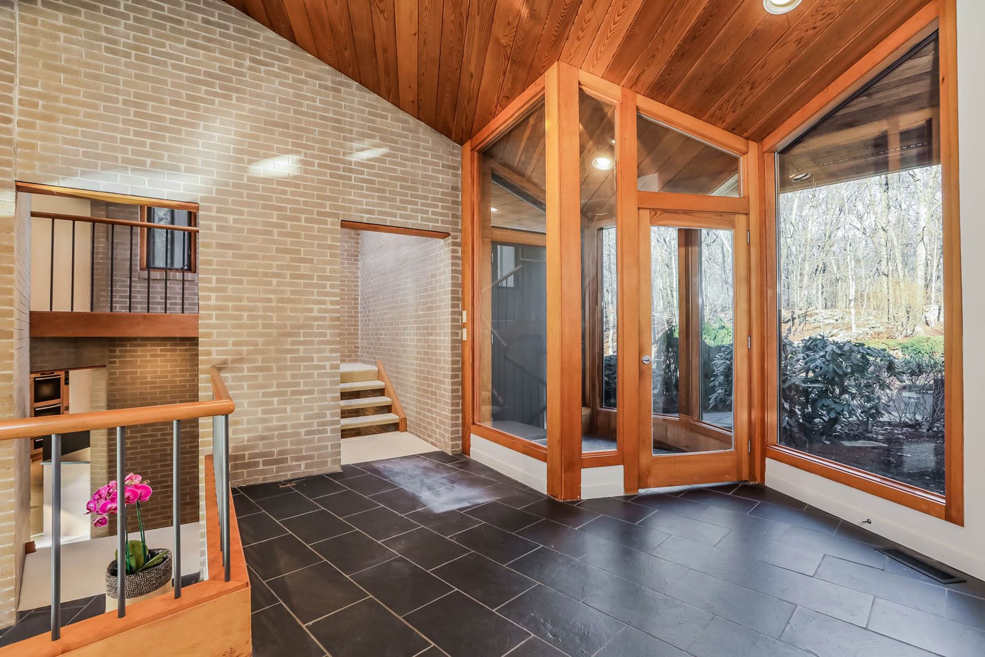 Glass entry vestibule with wood framing, slate flooring, and brick walls