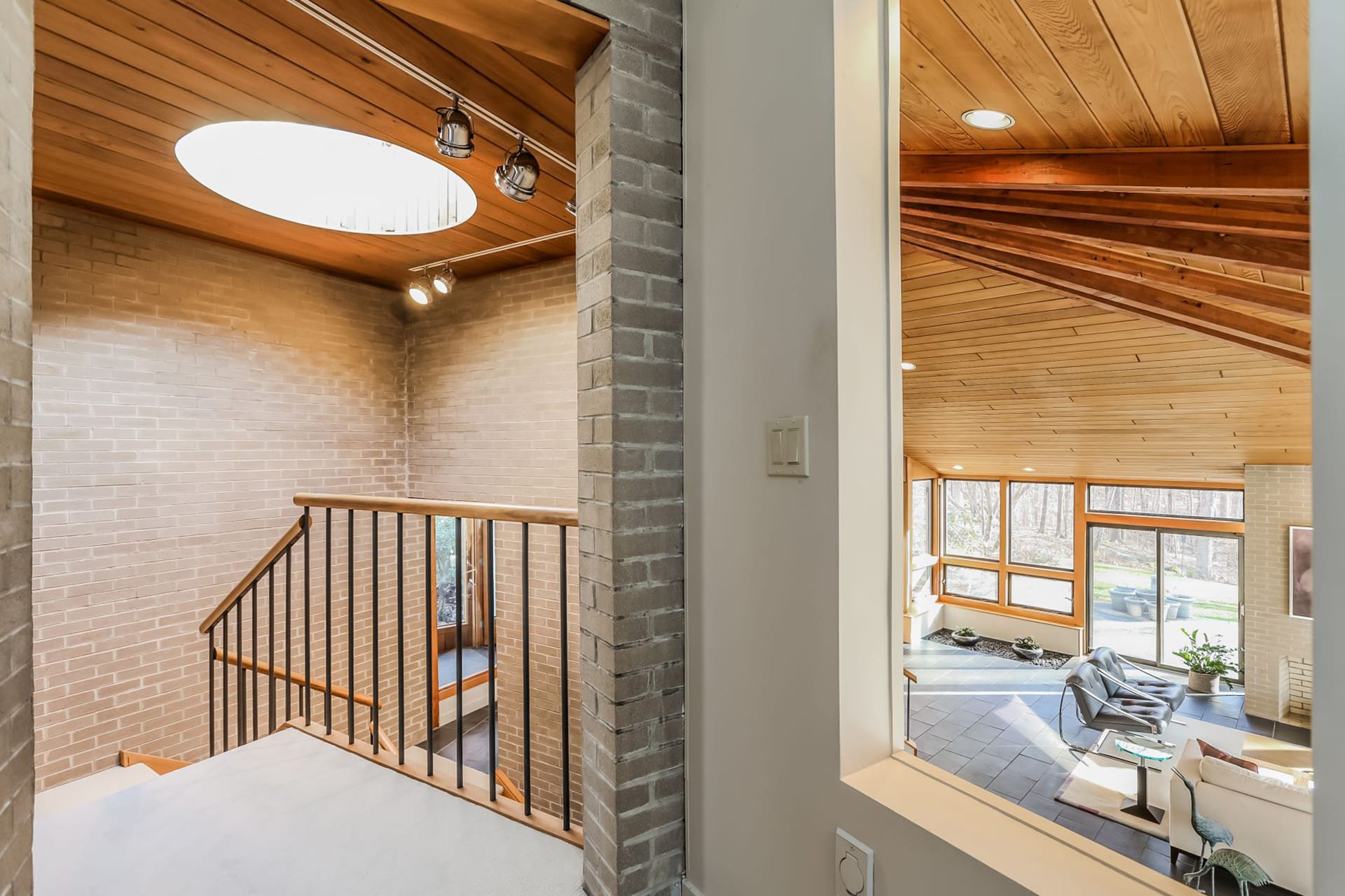 Upper level staircase landing with brick walls, wood paneled ceilings, and a skylight above