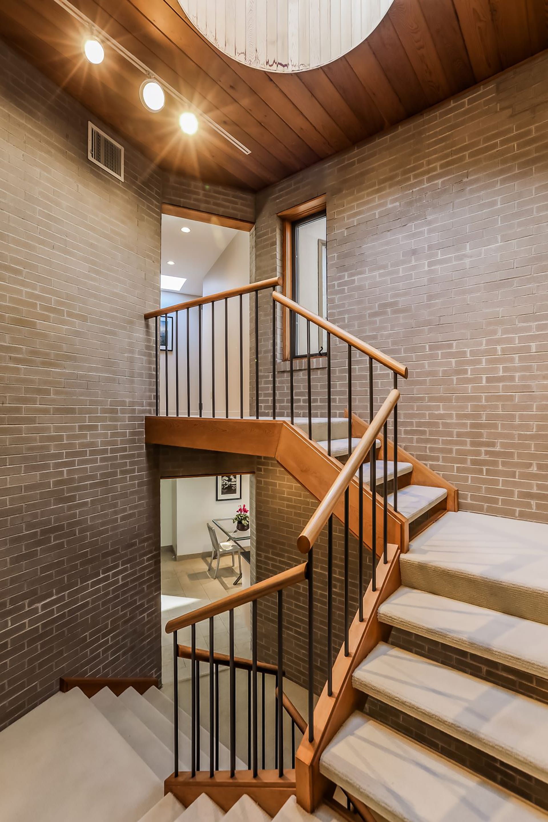 Open riser, open stringer staircase with brick walls, a skylight, and wood paneled ceilings