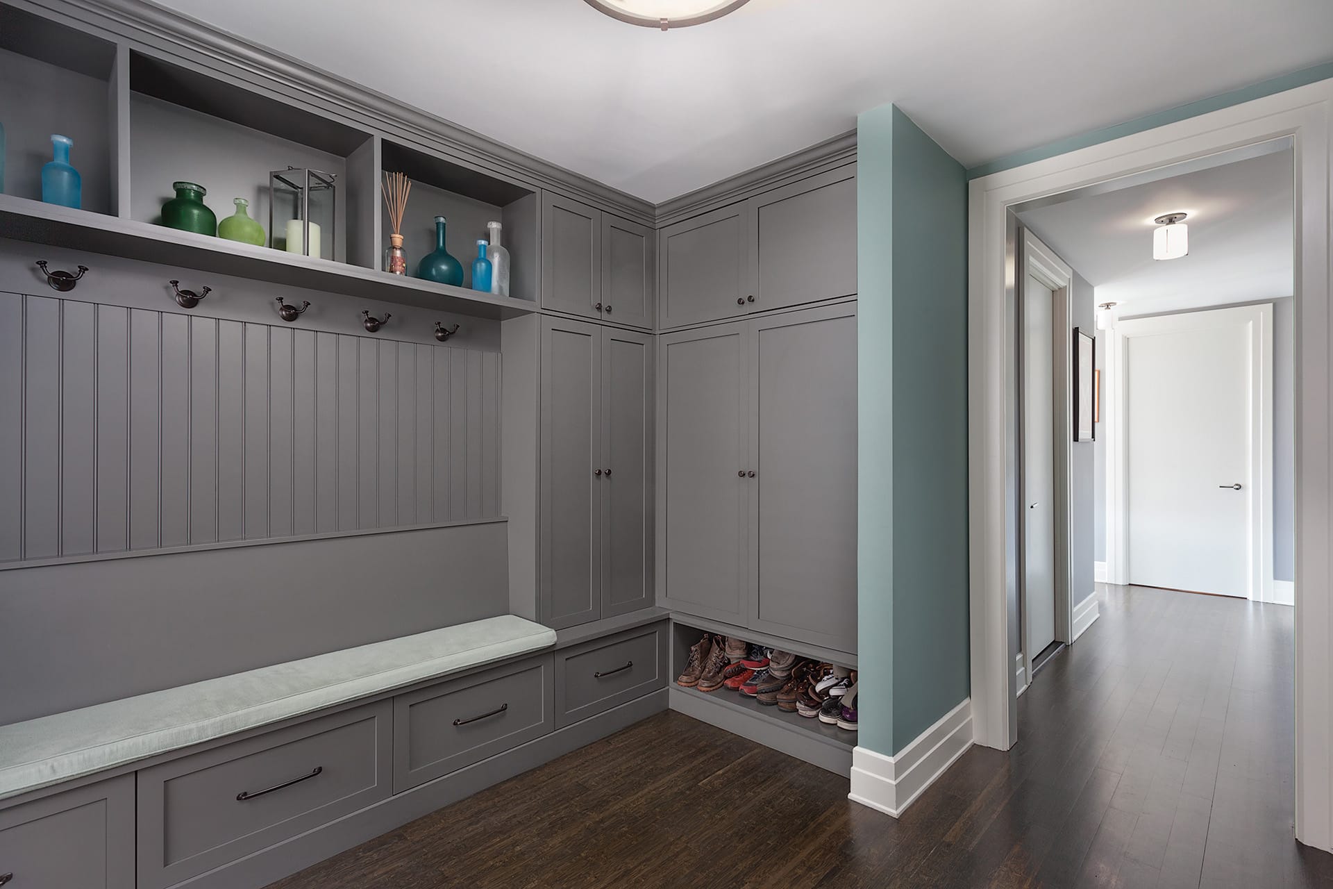 Grey custom millwork mudroom with teal accent wall and dark wood floors