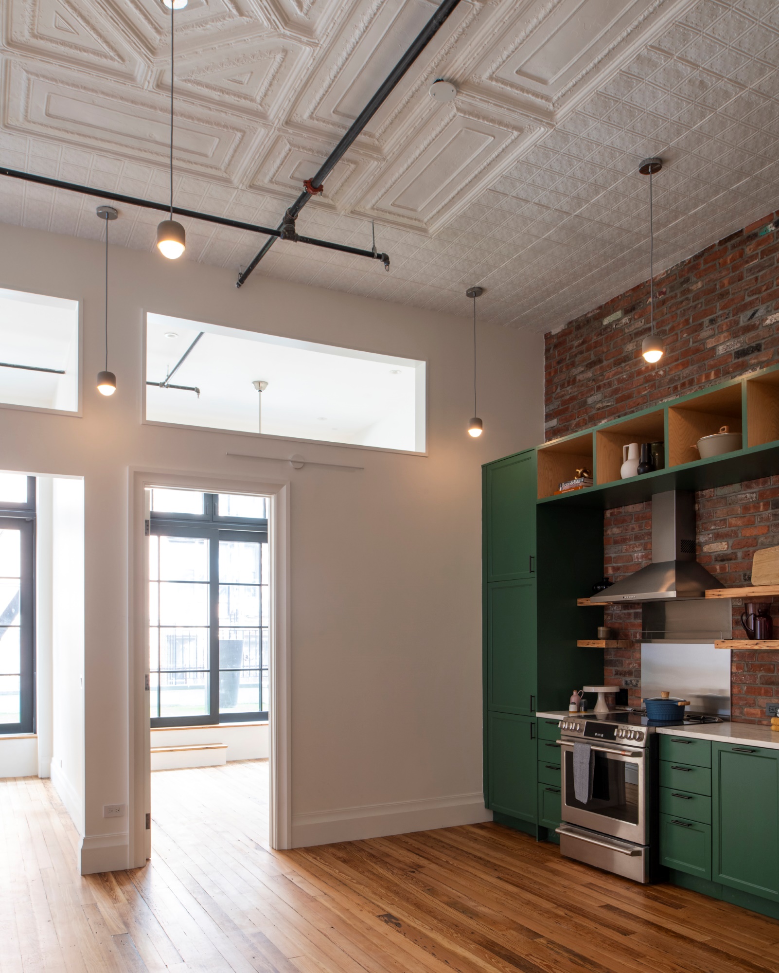 The kitchen of a Manhattan apartment with green millwork, stainless steel appliances, wood floors, and white painted tin ceilings.