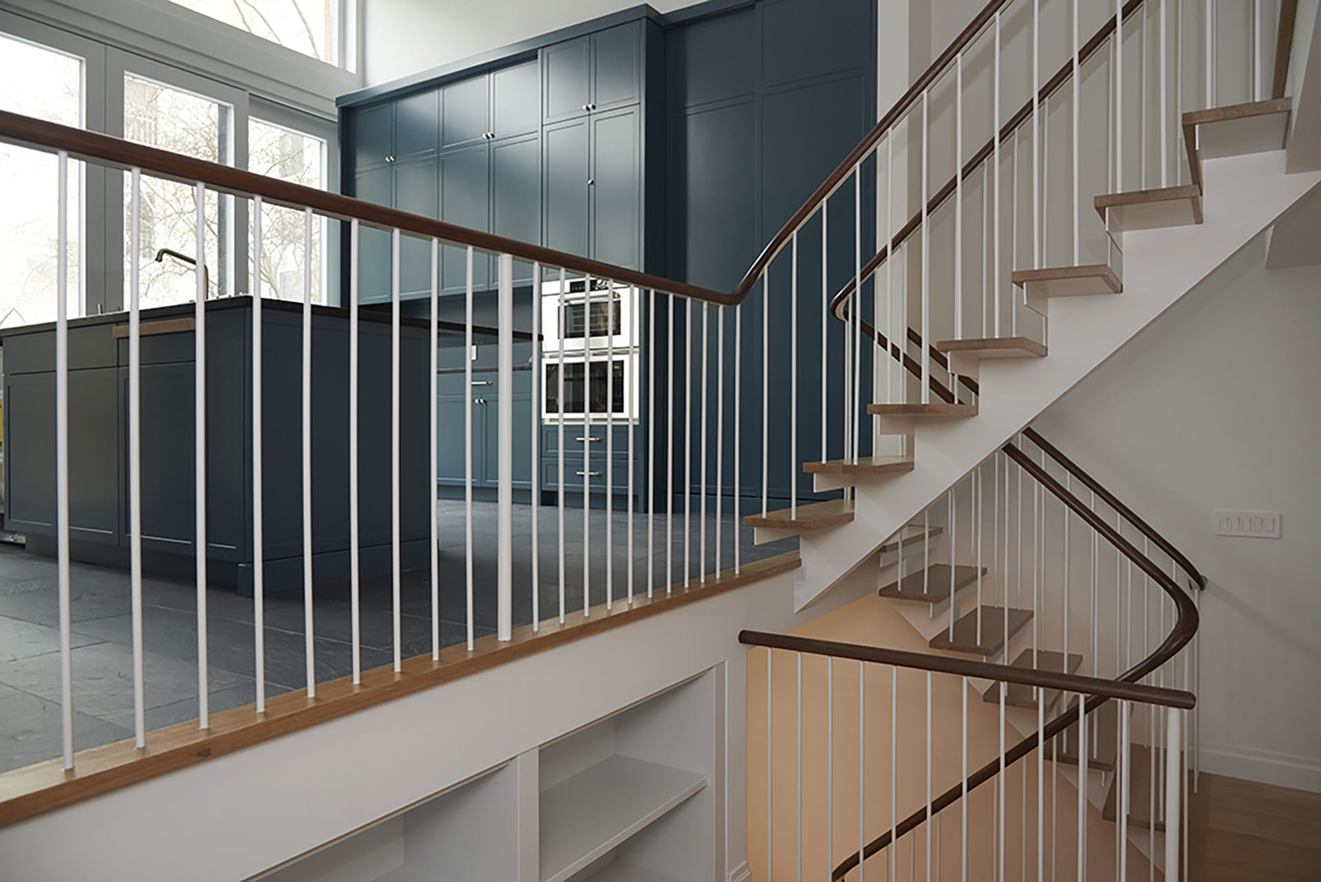 Split-level kitchen with dark teal cabinetry and a white and natural wood open staircase.