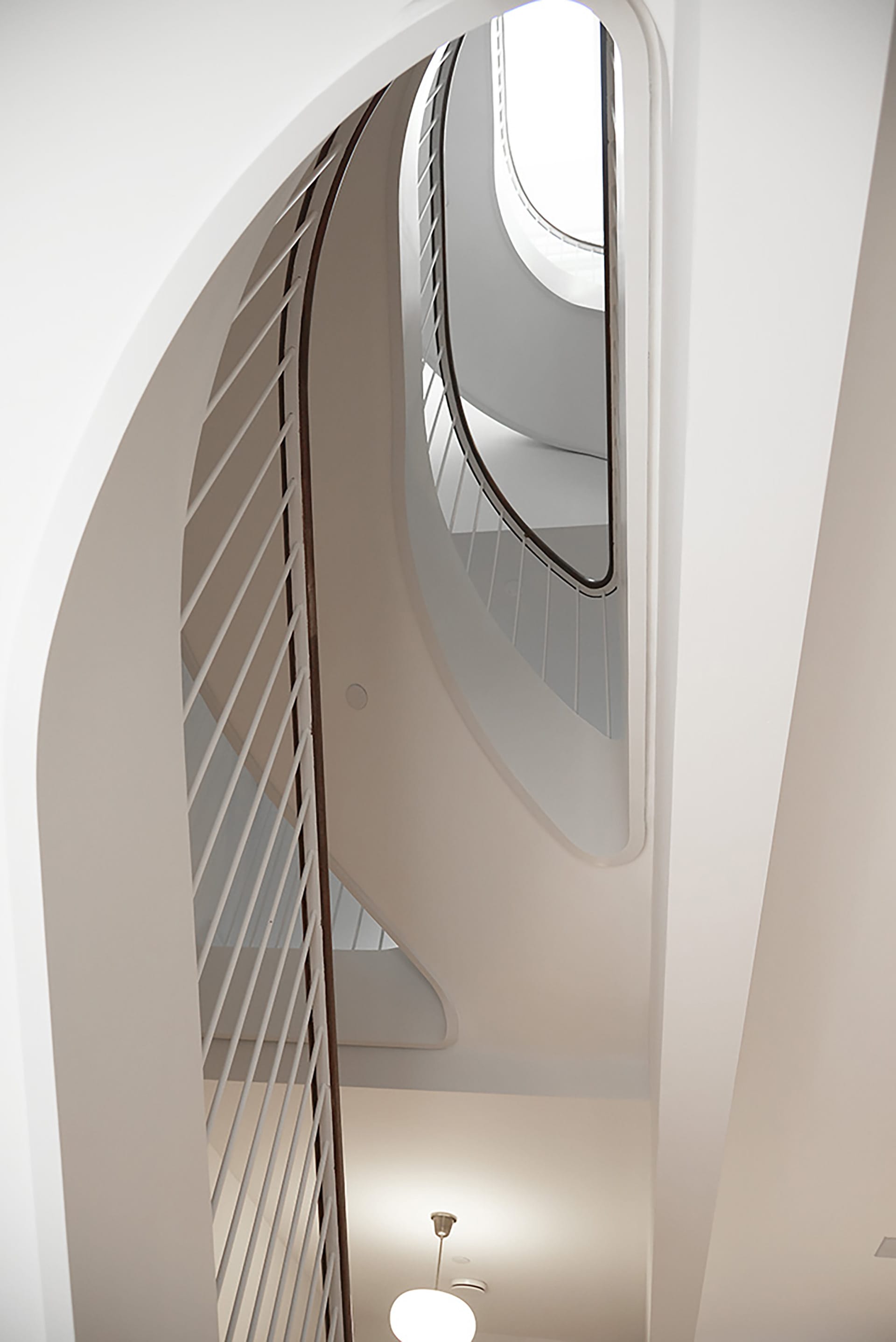 White sculptural staircase in a Brooklyn Heights Passive House. Three stories of the staircase are viewed from below.