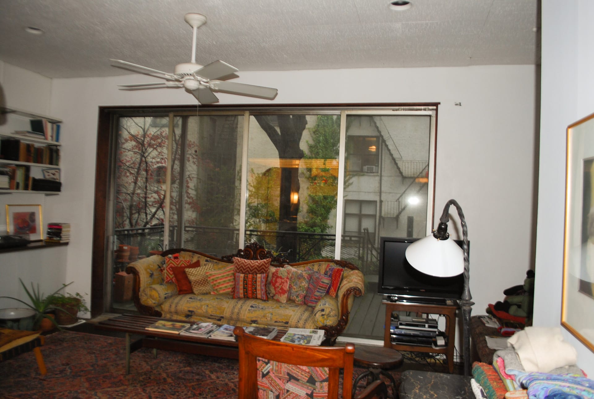 Living room with a patterned couch, ceiling fan, and sliding glass doors to the rear yard. An armchair and floor lamp sit in the foreground.