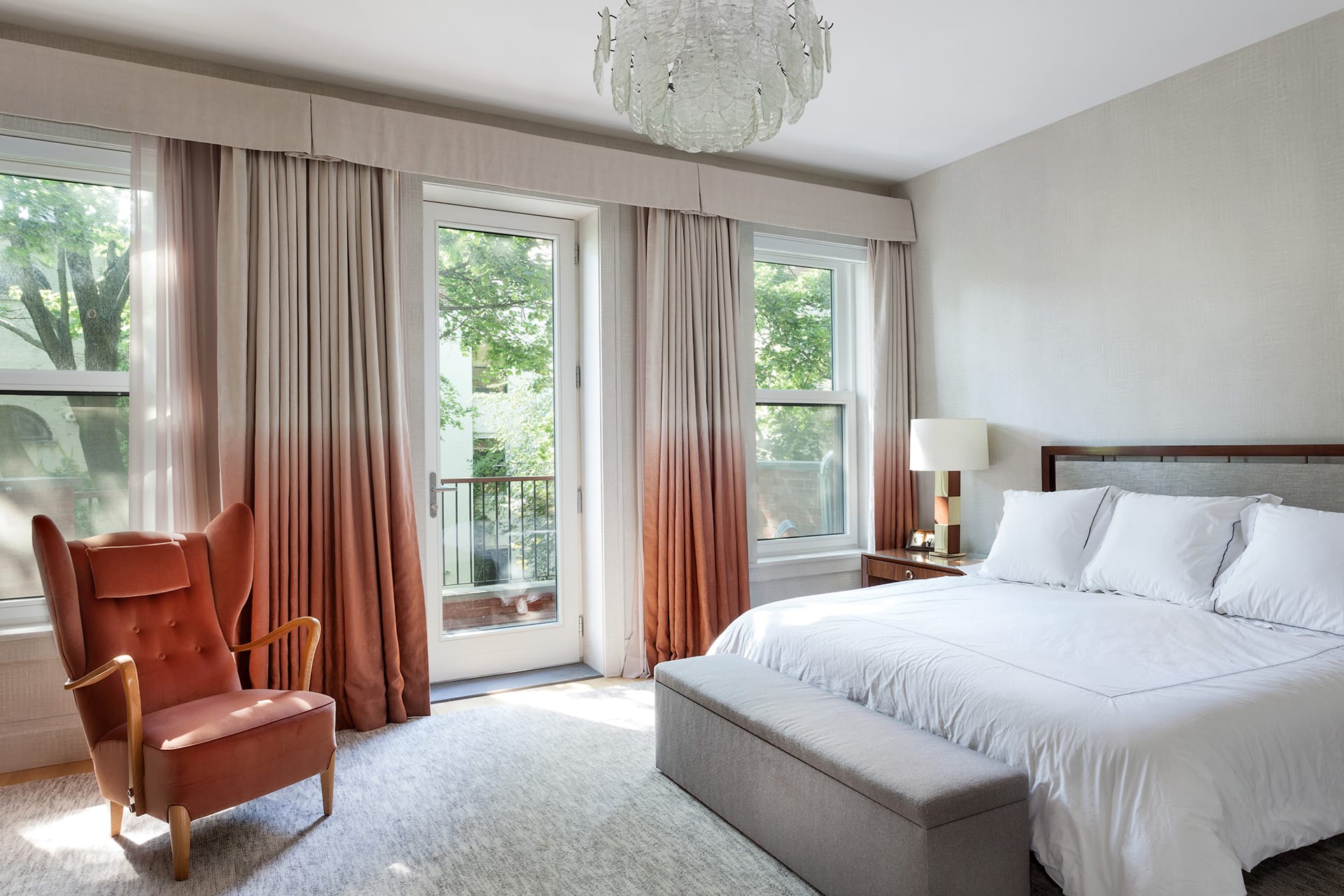 Primary bedroom with a large chandelier, juliet balcony, and ombre curtains.