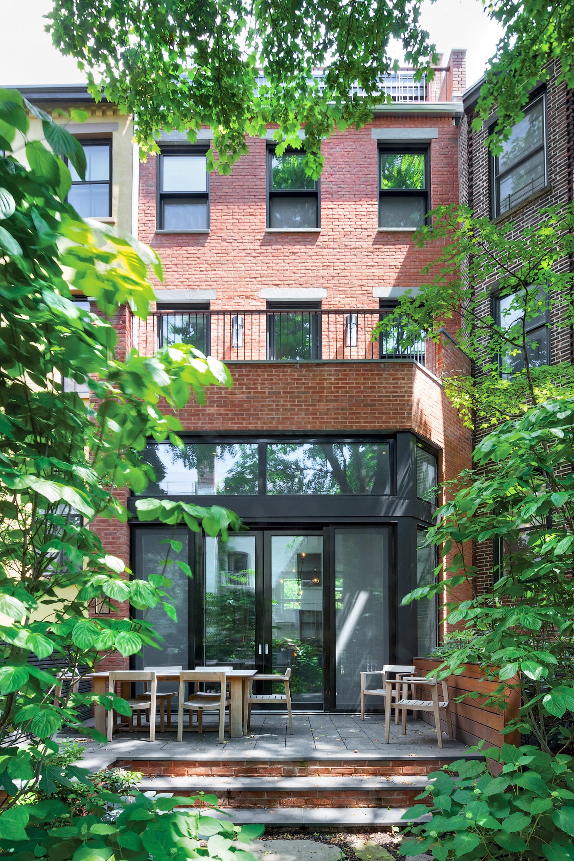 Rear facade of a Brooklyn Heights townhouse with a second-story roof deck atop an extension and large glass windows and doors below.