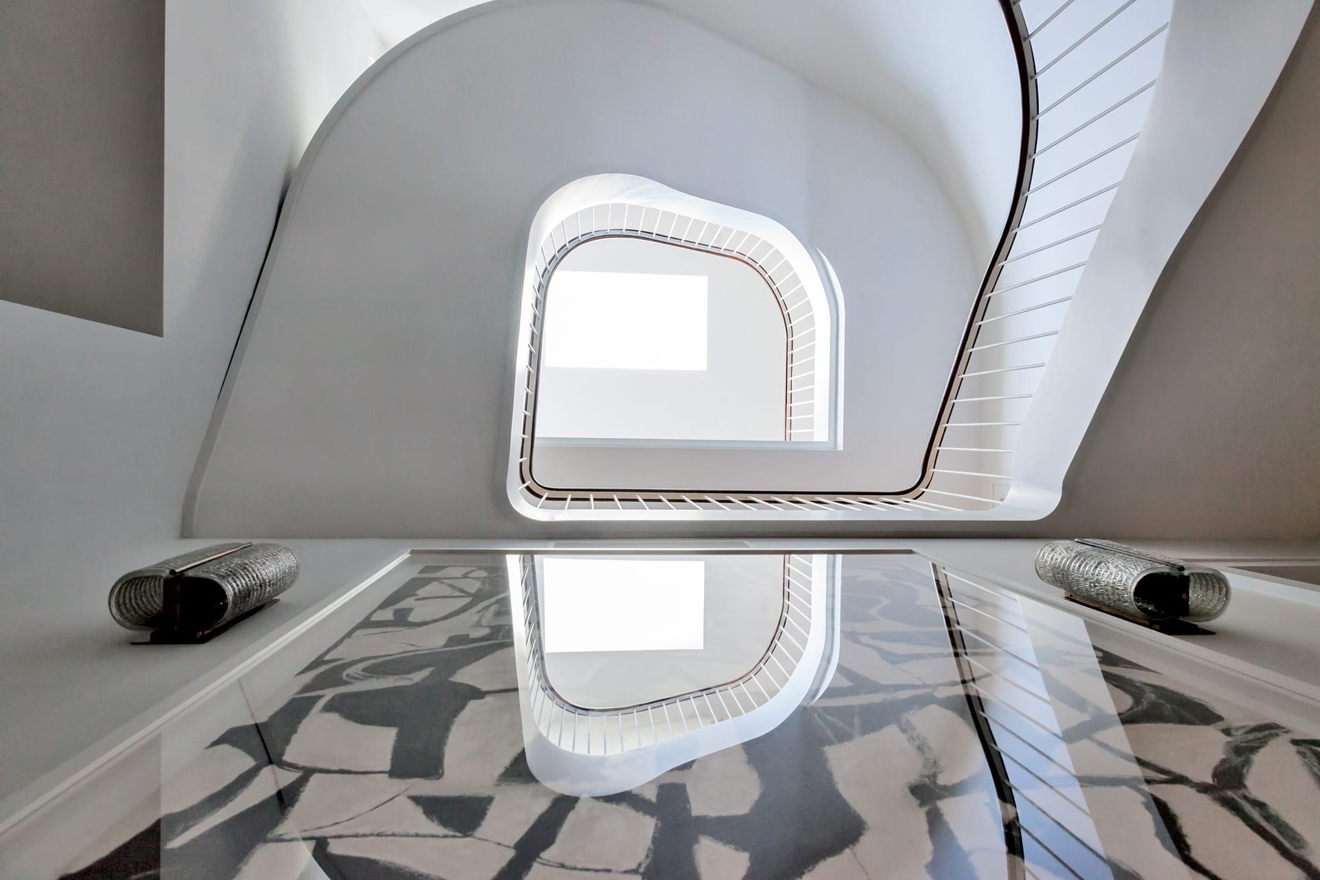 View of a multistory sculptural staircase from below with a skylight on the top floor.