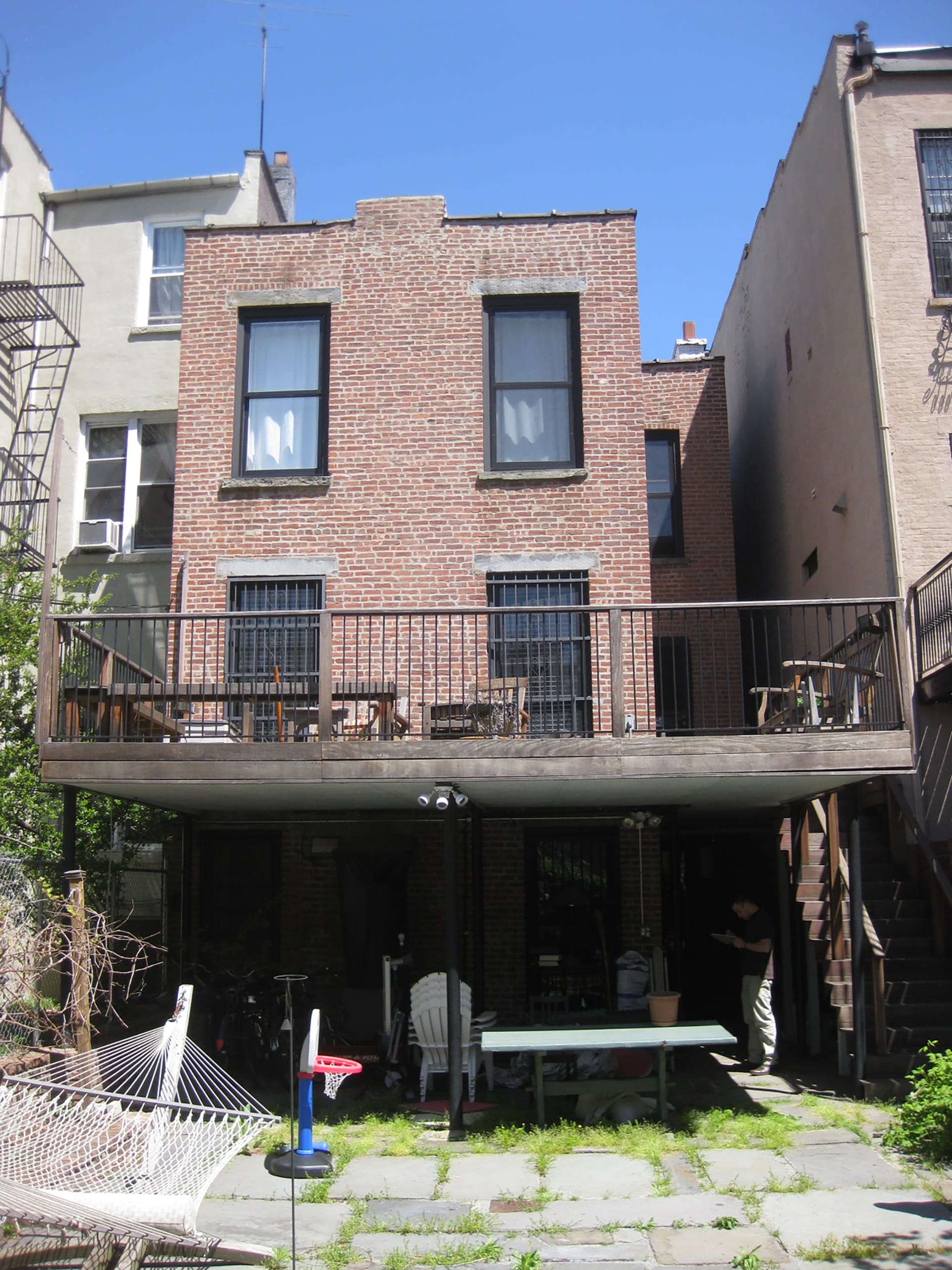 Rear facade of a brick townhouse in Carroll Gardens with small windows and a suspended deck before our renovation.