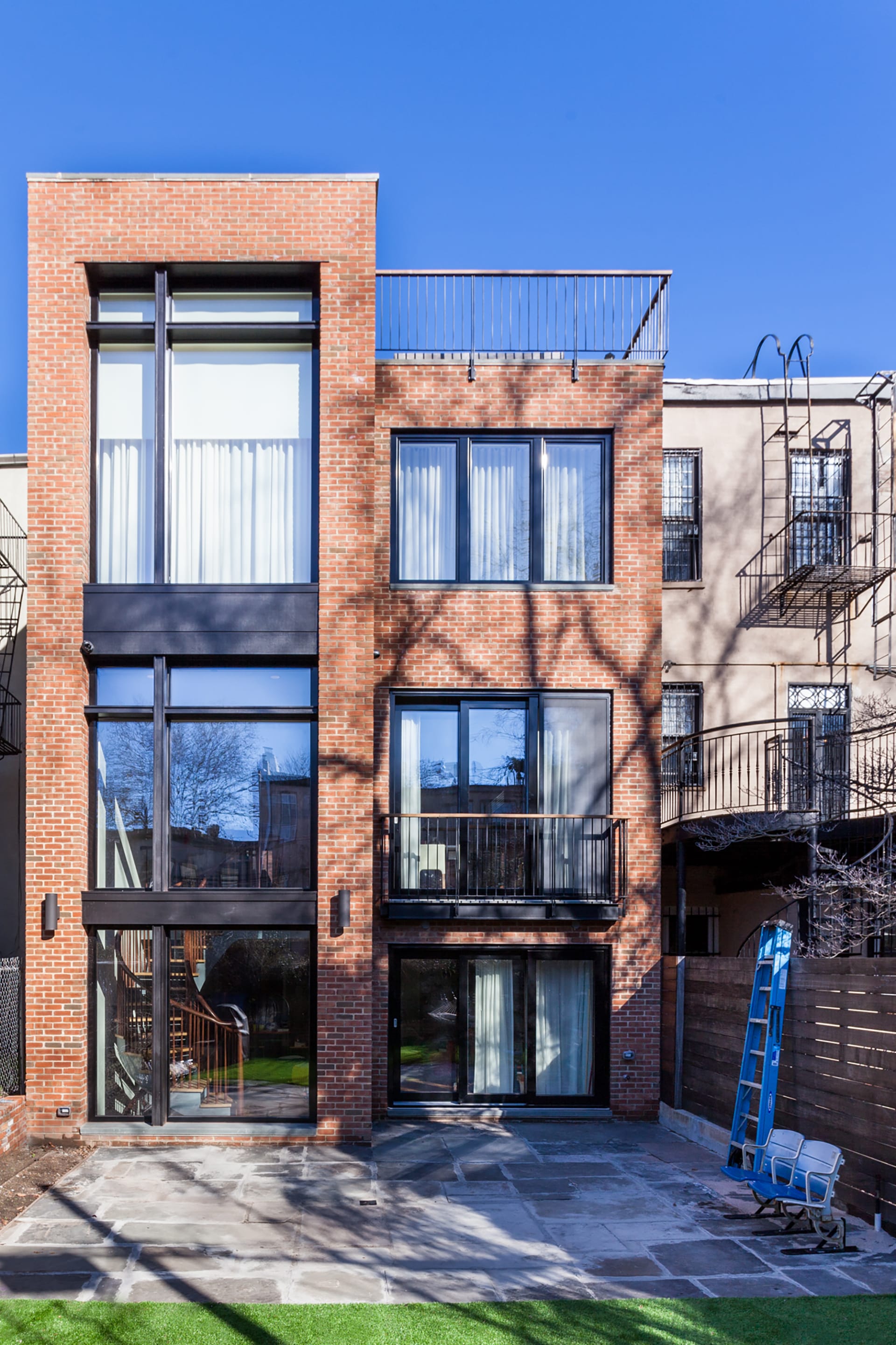 Rear facade of a brick townhouse with large expanses of glass, a rooftop balcony, and large sliding glass doors