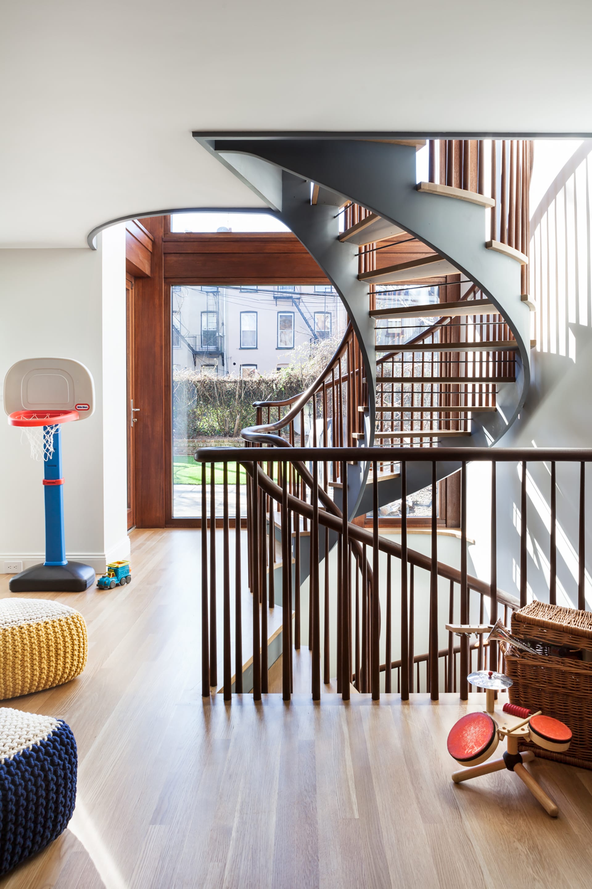 Sculptural staircase with open stringers and open risers in front of large, floor to ceiling windows.