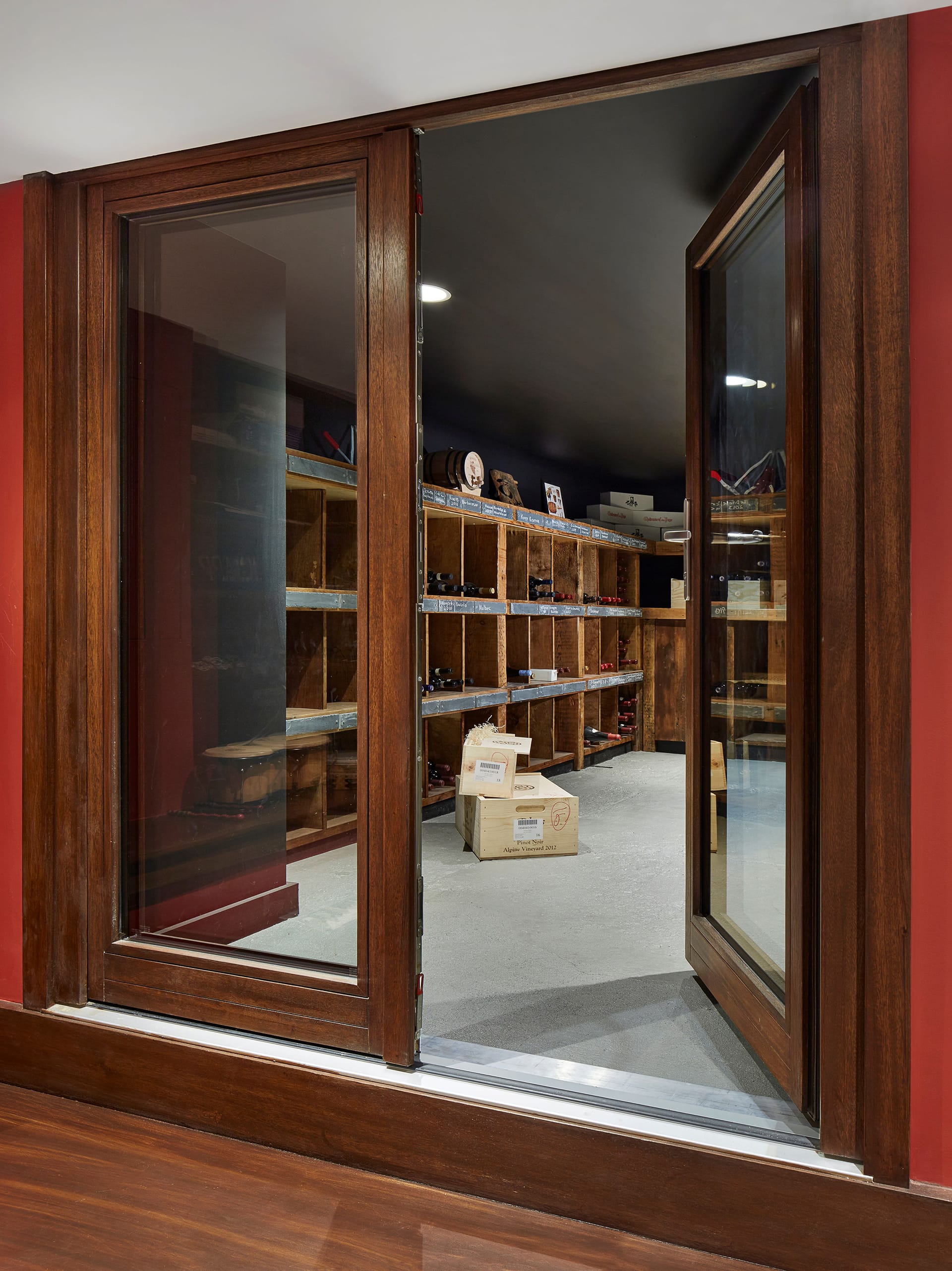 Wine room with large, dark wood doors, reclaimed wood storage cubbies, and light grey floors.