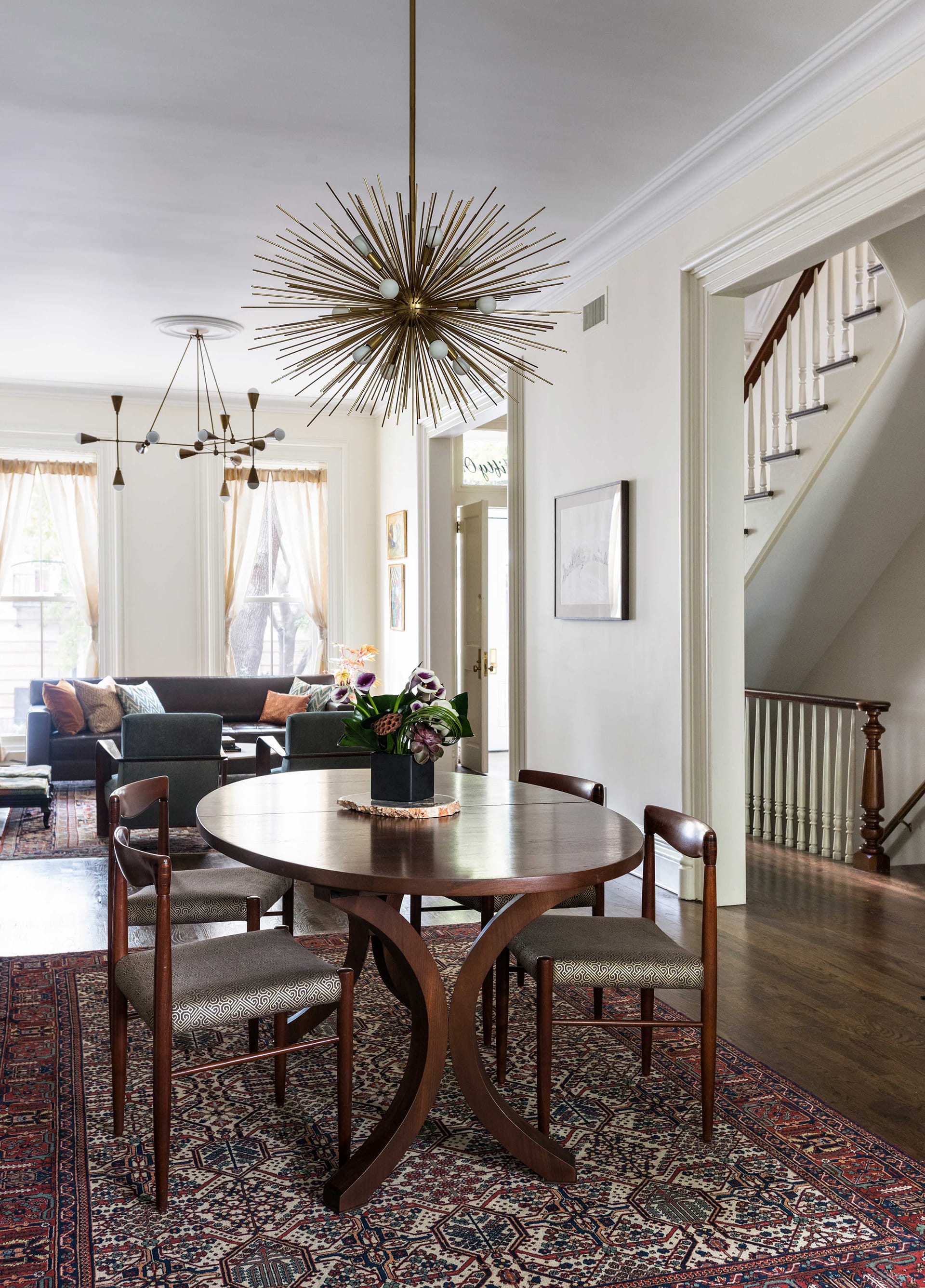 Dining and living area with dark wood floors, two oriental rugs, and modern chandeliers