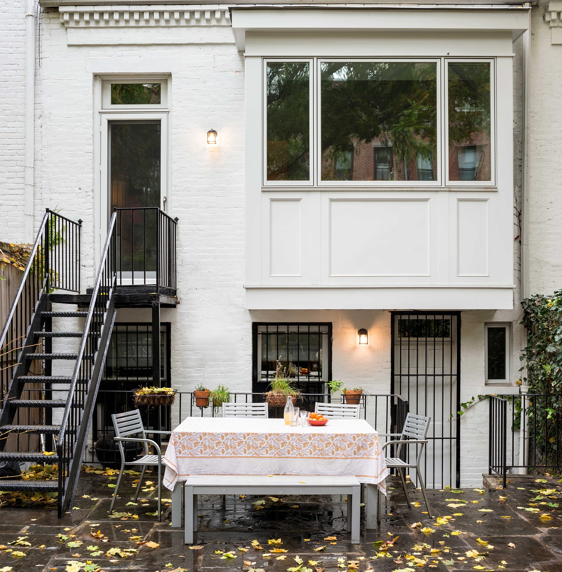 Rear facade with extended bay window, new staircase, and picnic table. Yellow leaves dot the stone paved rear yard