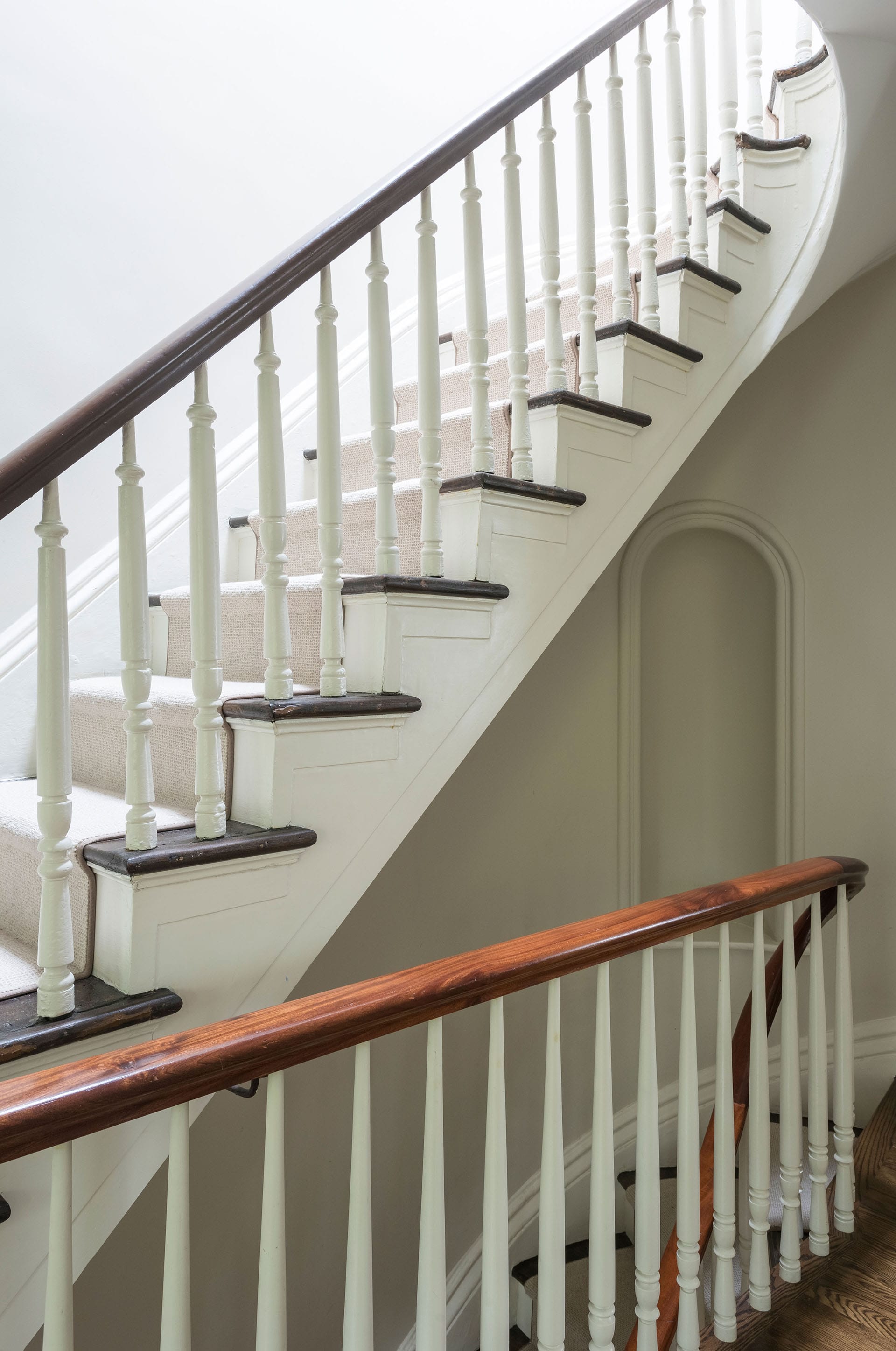 Sculptural staircase with a white stair runner, wood handrail, and a niche on the wall