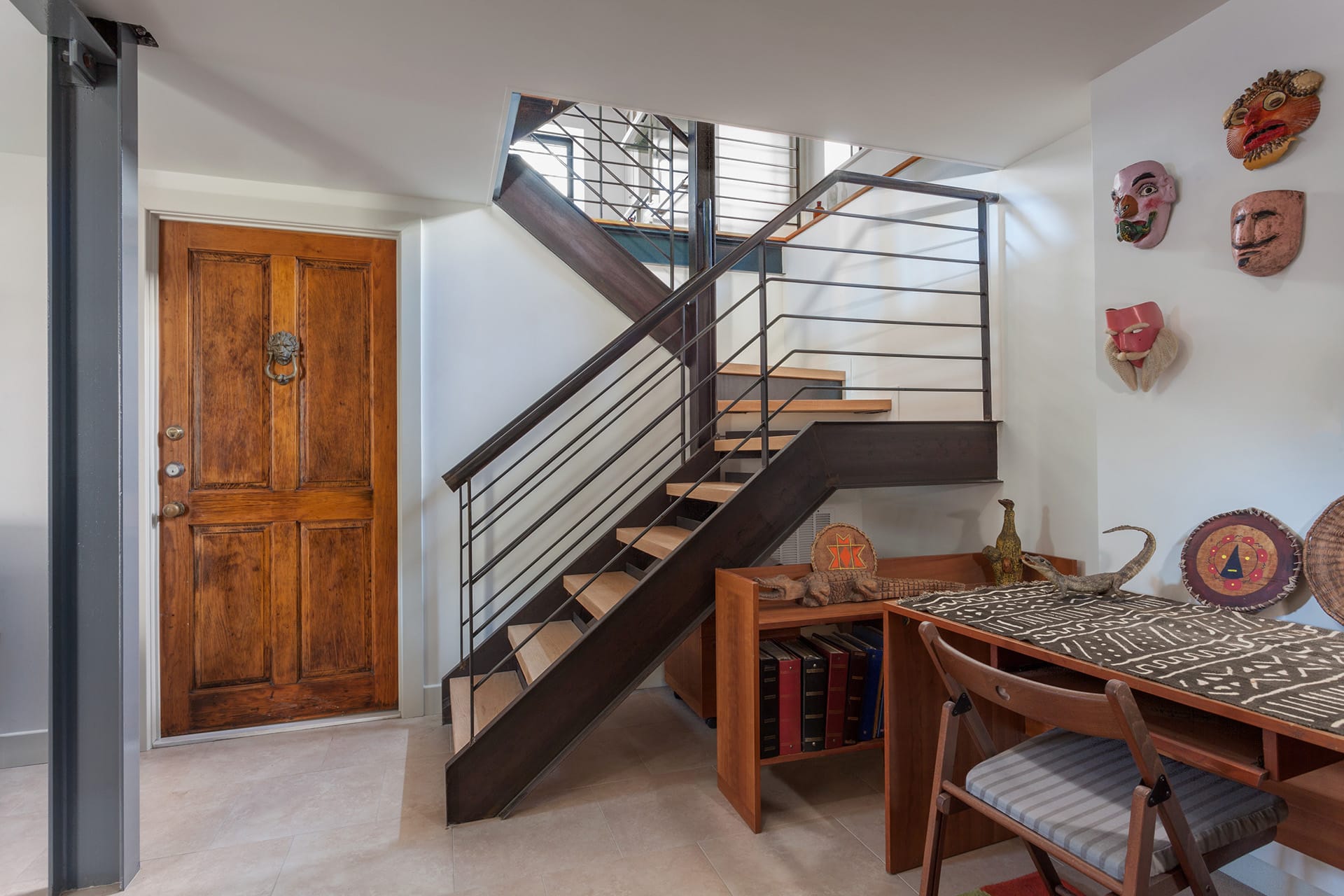 Metal staircase with wood risers, a historical door, and masks and sculptures in the basement of a Cobble Hill carriage house