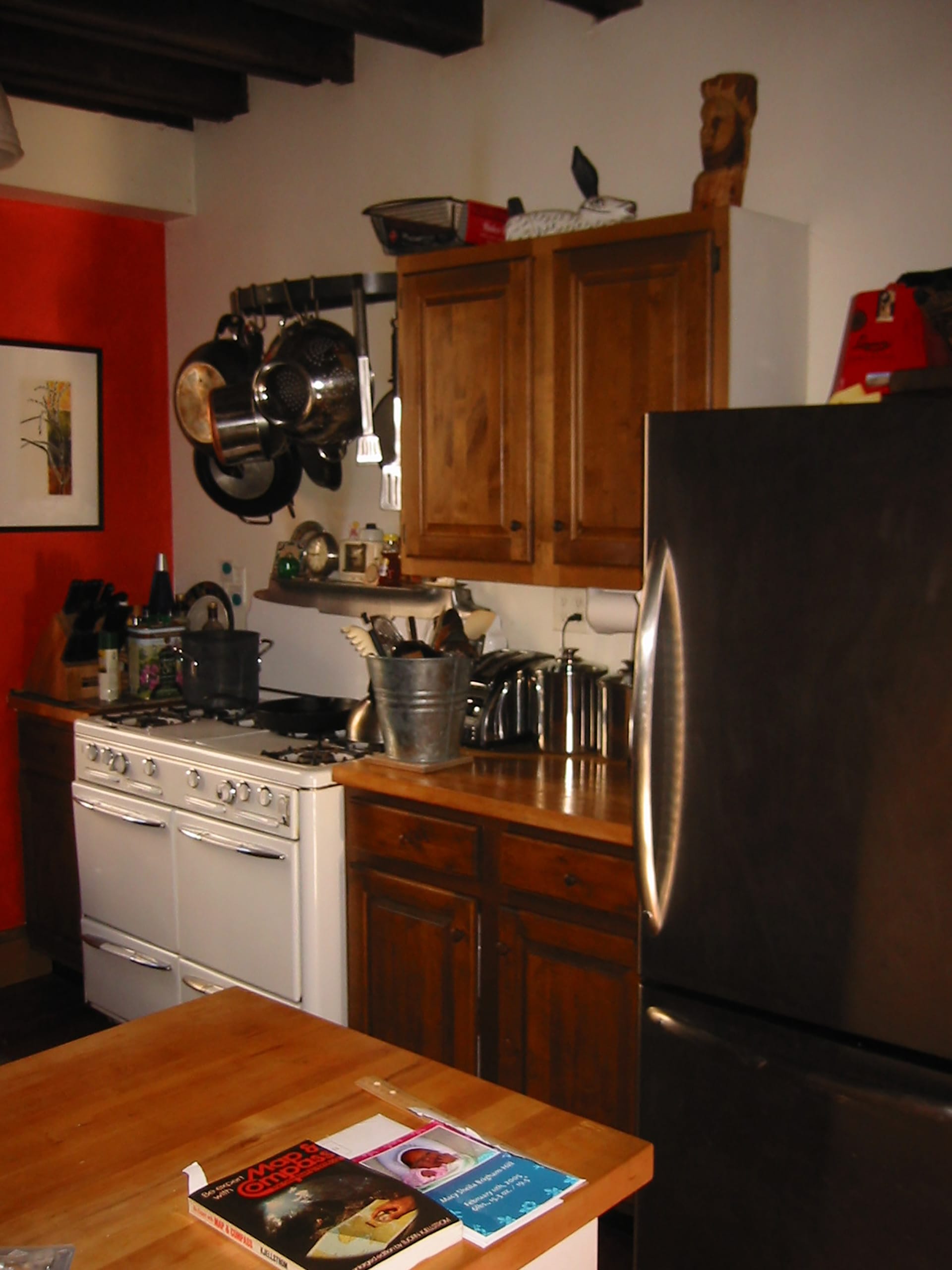 Kitchen of a carriage house before renovation with a red accent wall, white range, wood cabinets, and stainless steel refrigerator