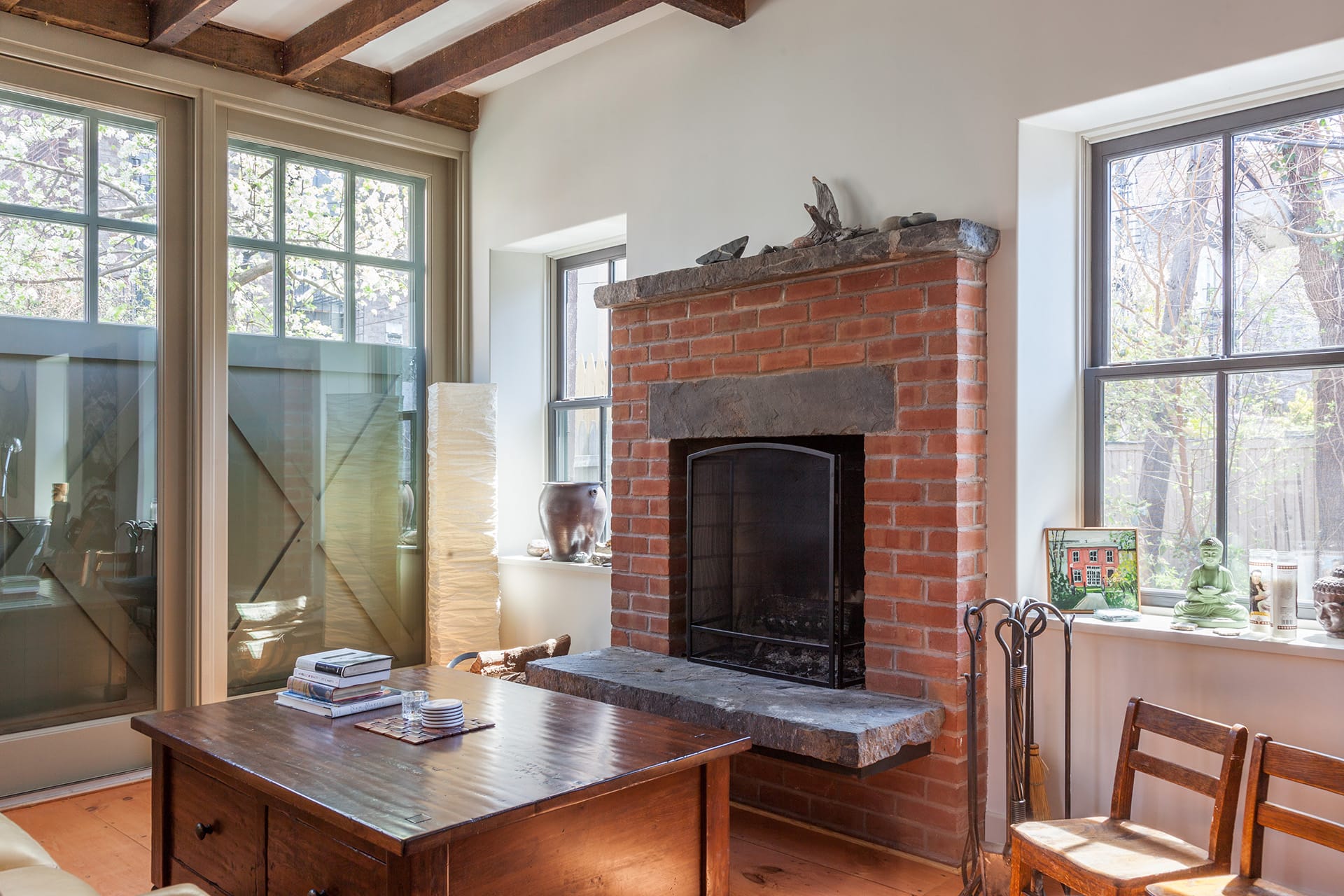 Living space in a carriage house with a wall of glass doors covered by sliding barn doors, exposed beams, and original fireplace.