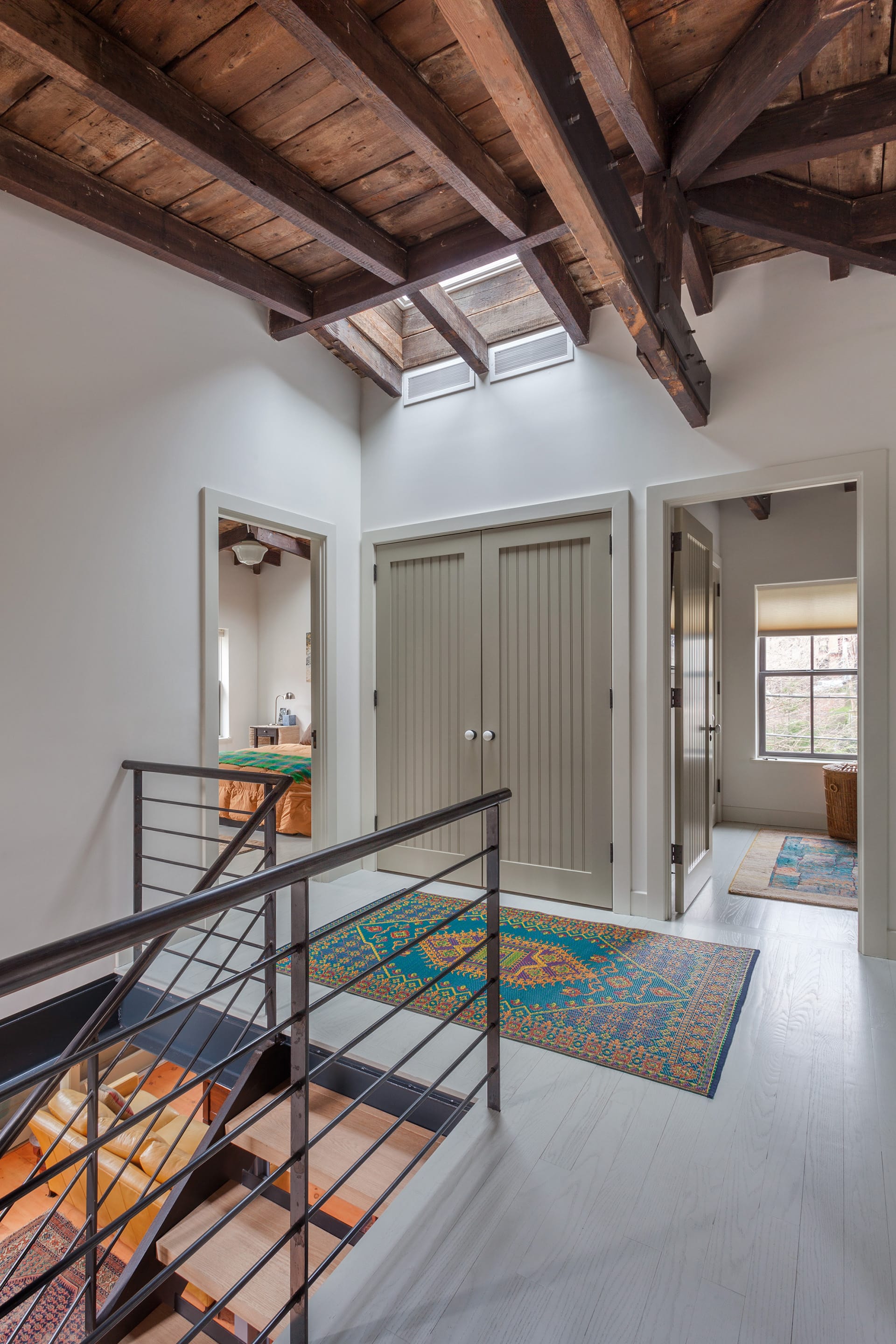 Second-floor stair landing with exposed ceiling beams, a skylight above the staircase, and grey wood floors.