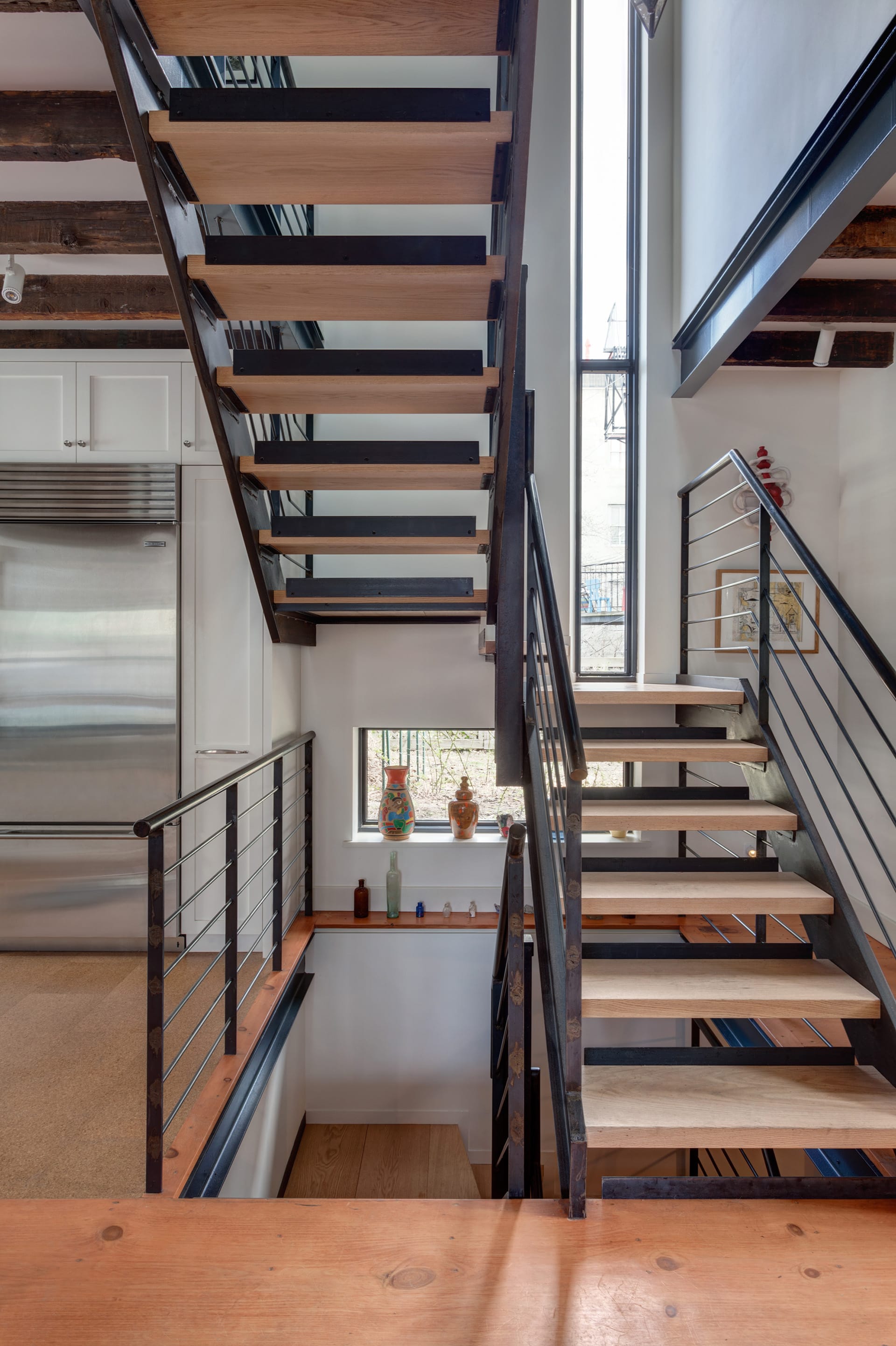 Open stringer, open riser metal and wood staircase with a long, skinny window at the landings.