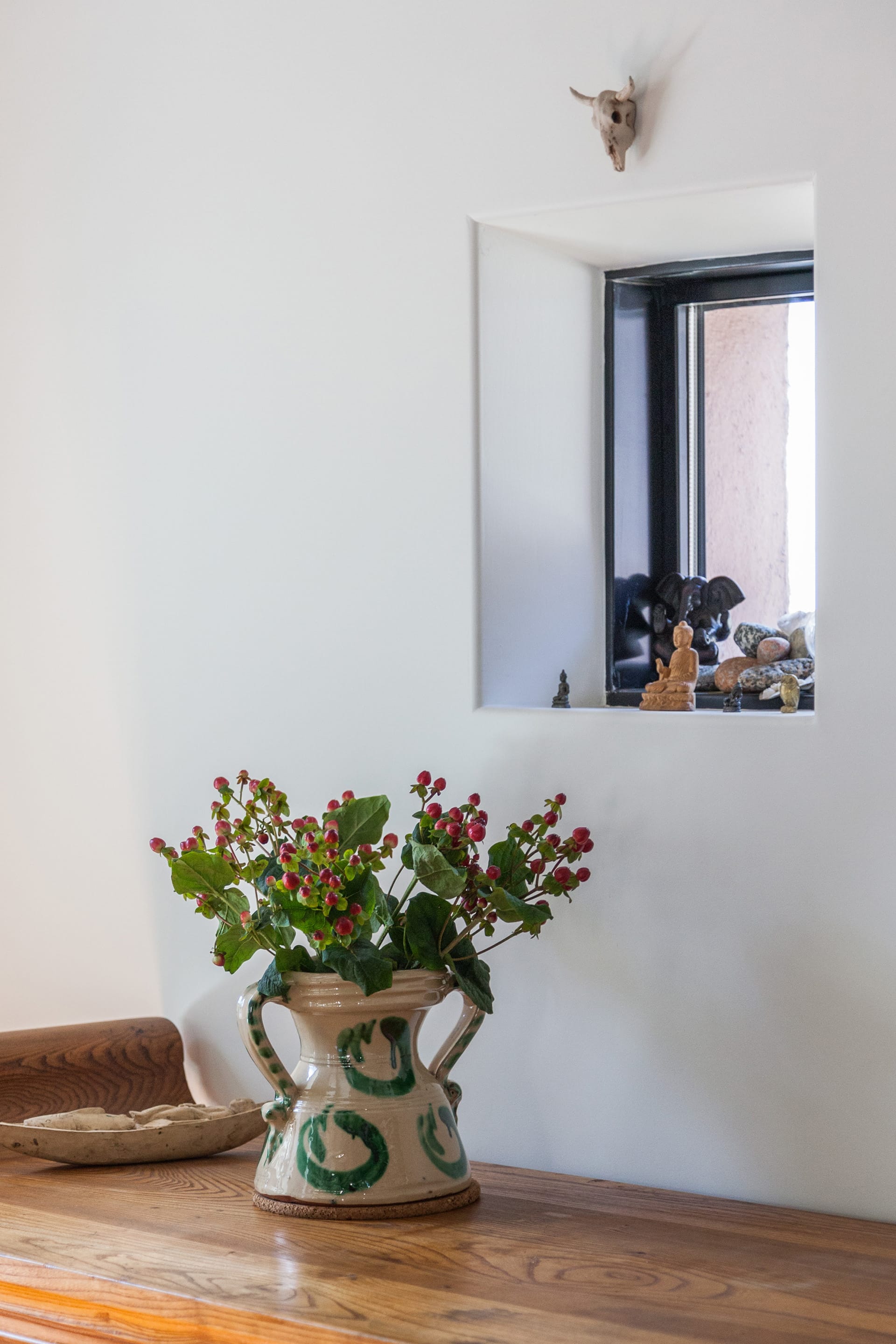 A bundle of roses in a large ceramic planter in front of a window. Various statuettes sit on the windowsill.