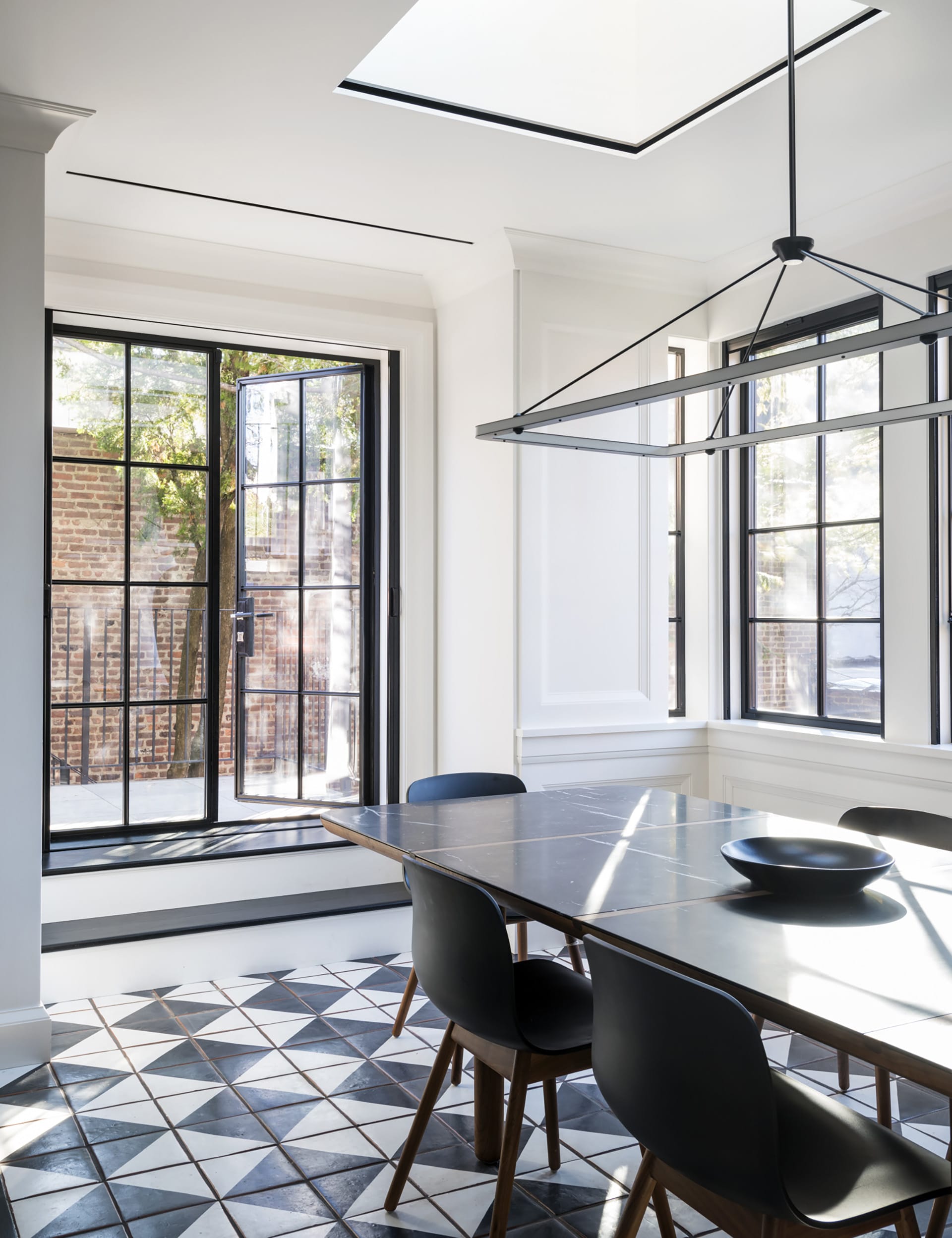 Dining area at the rear of a Brooklyn Heights townhouse with glass doors, large windows, a skylight, and checkered floors.