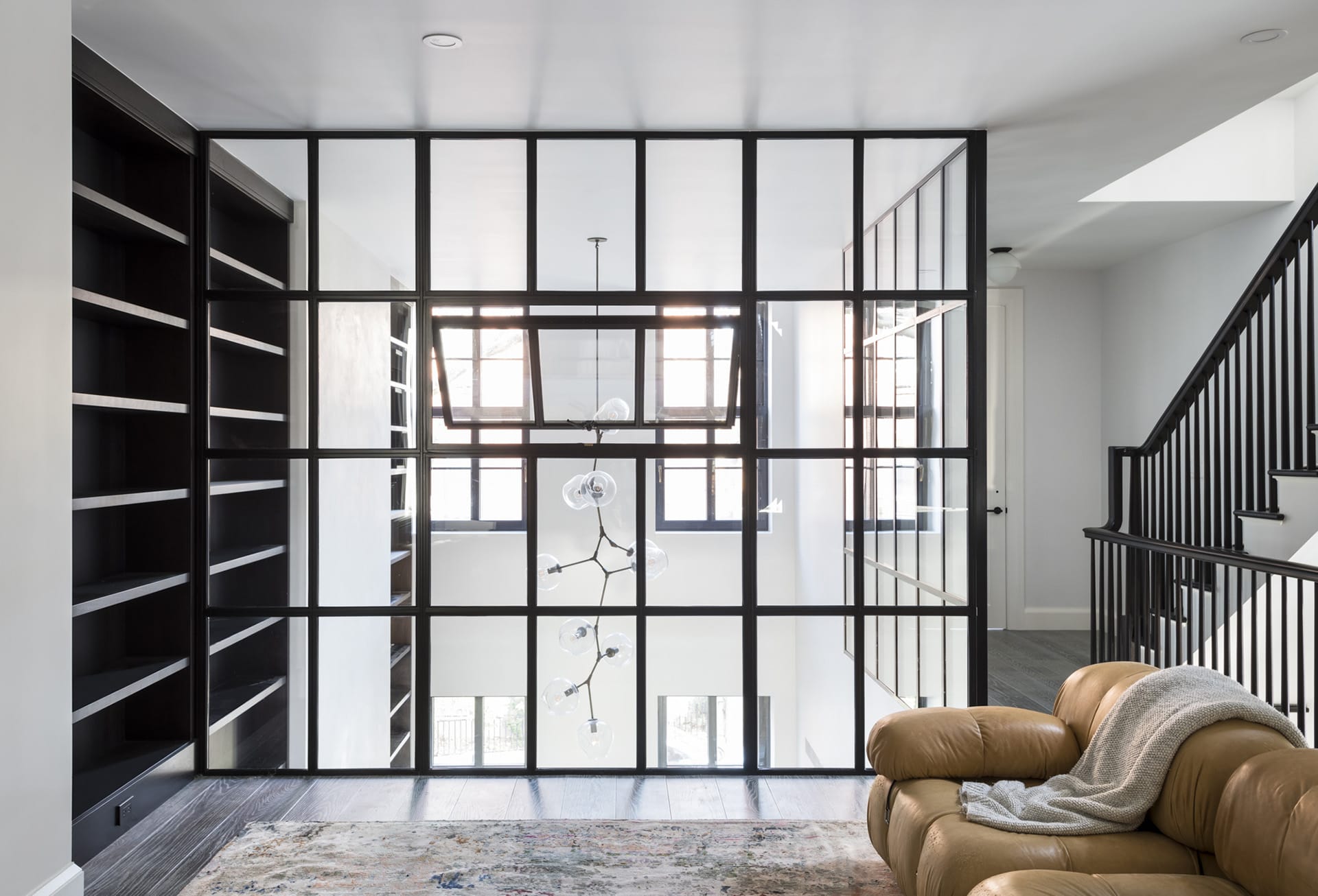 Glass wall system separating a double-height living room from a second-floor seating area
