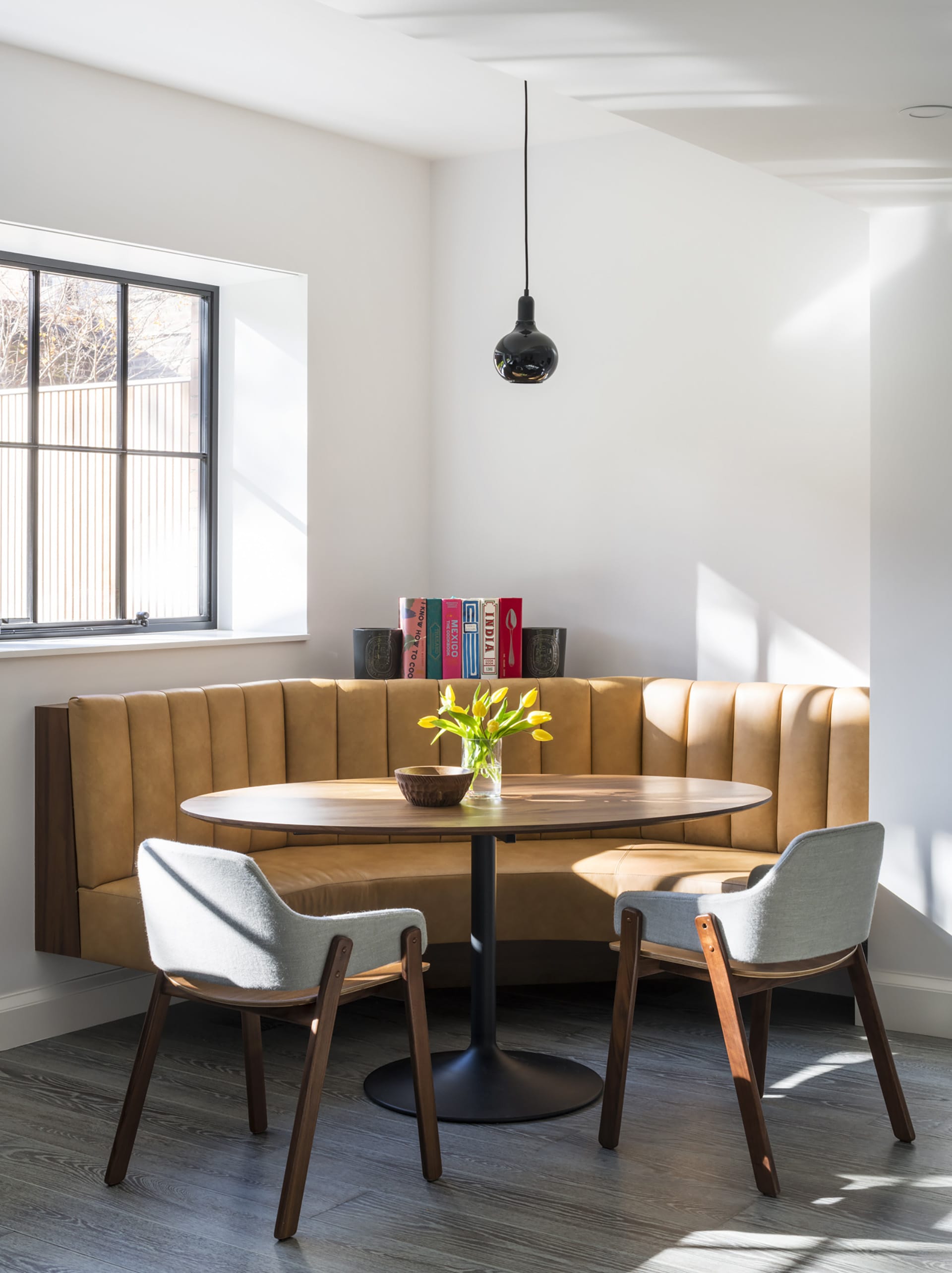 Leather banquette with two grey chairs and a black pendant light in the garden apartment of a Brooklyn Heights townhouse