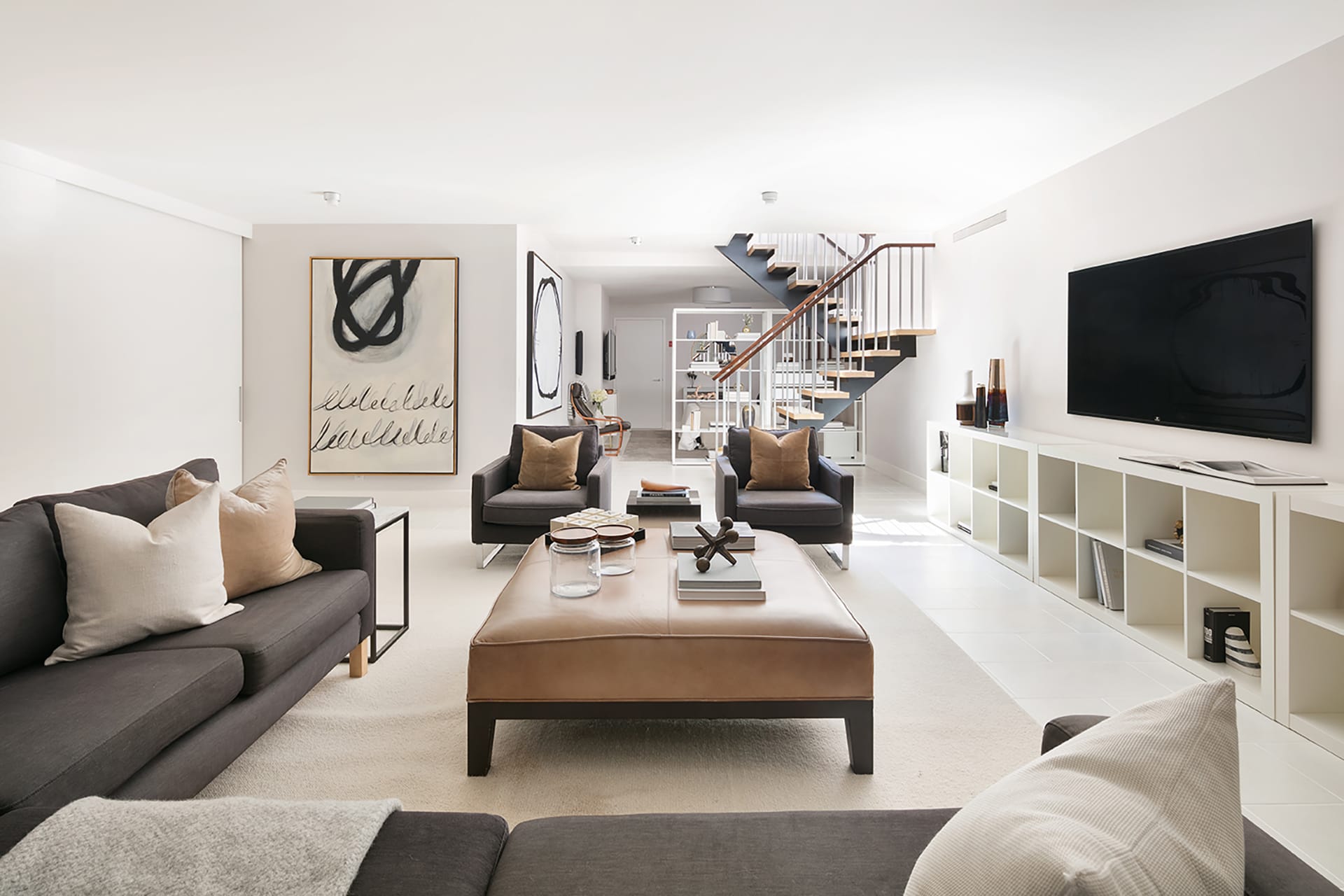 Basement-level den with grey chairs and a leather ottoman