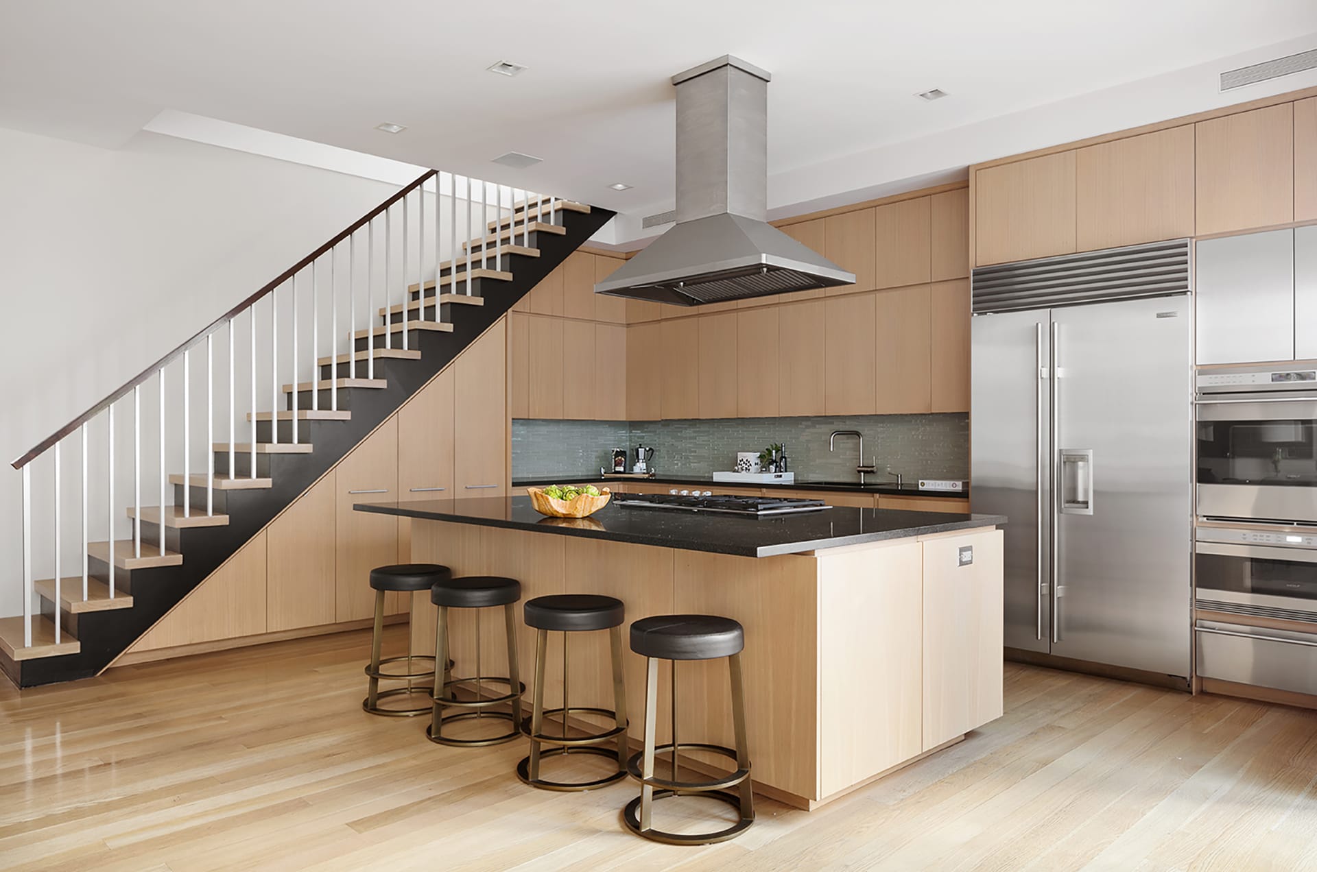 Kitchen with custom light wood cabinetry, stainless steel appliances, and four flack barstools