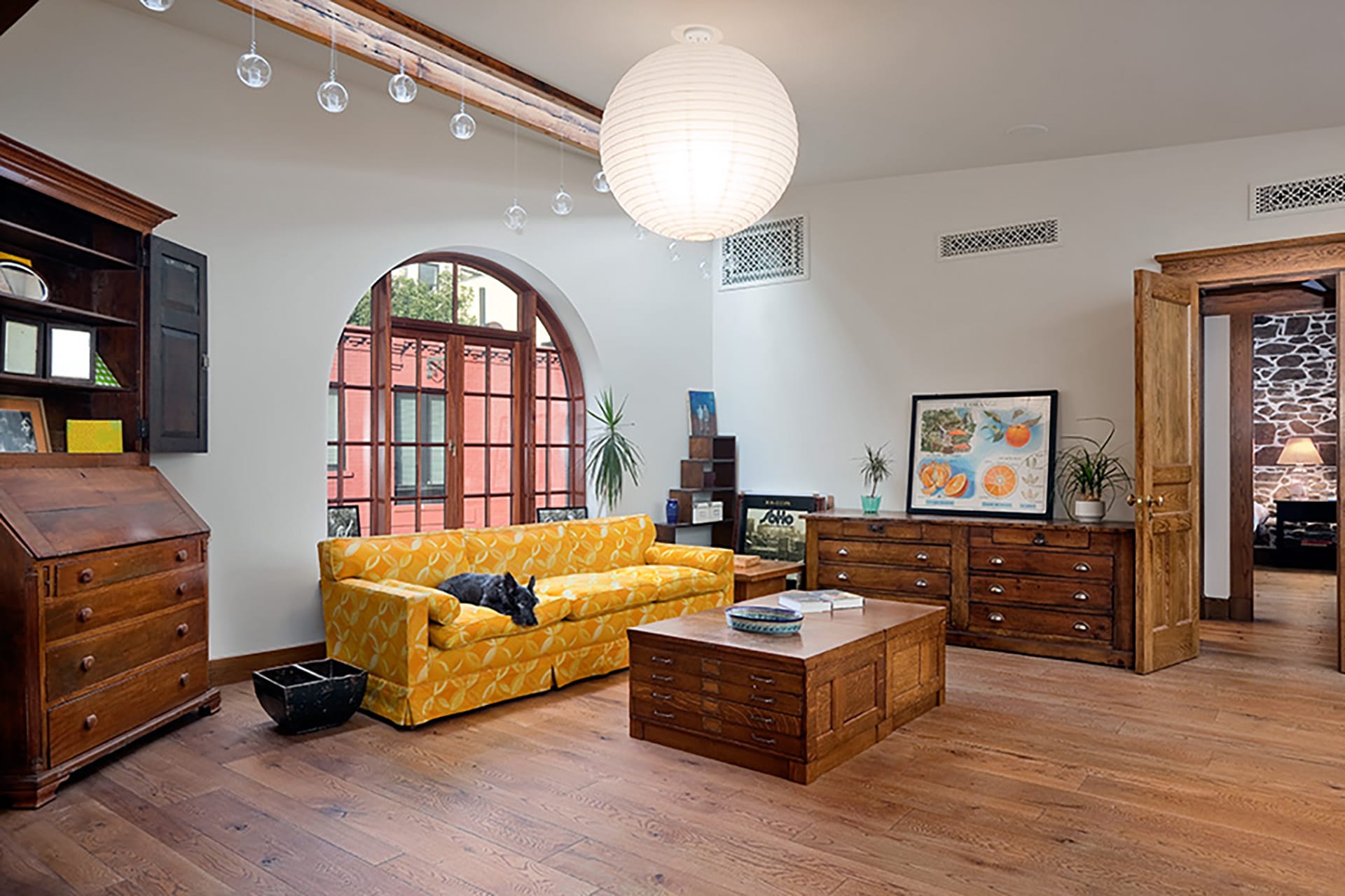 Yellow couch in front of a round window with traditional wood furnishings and a large spherical light fixtures.