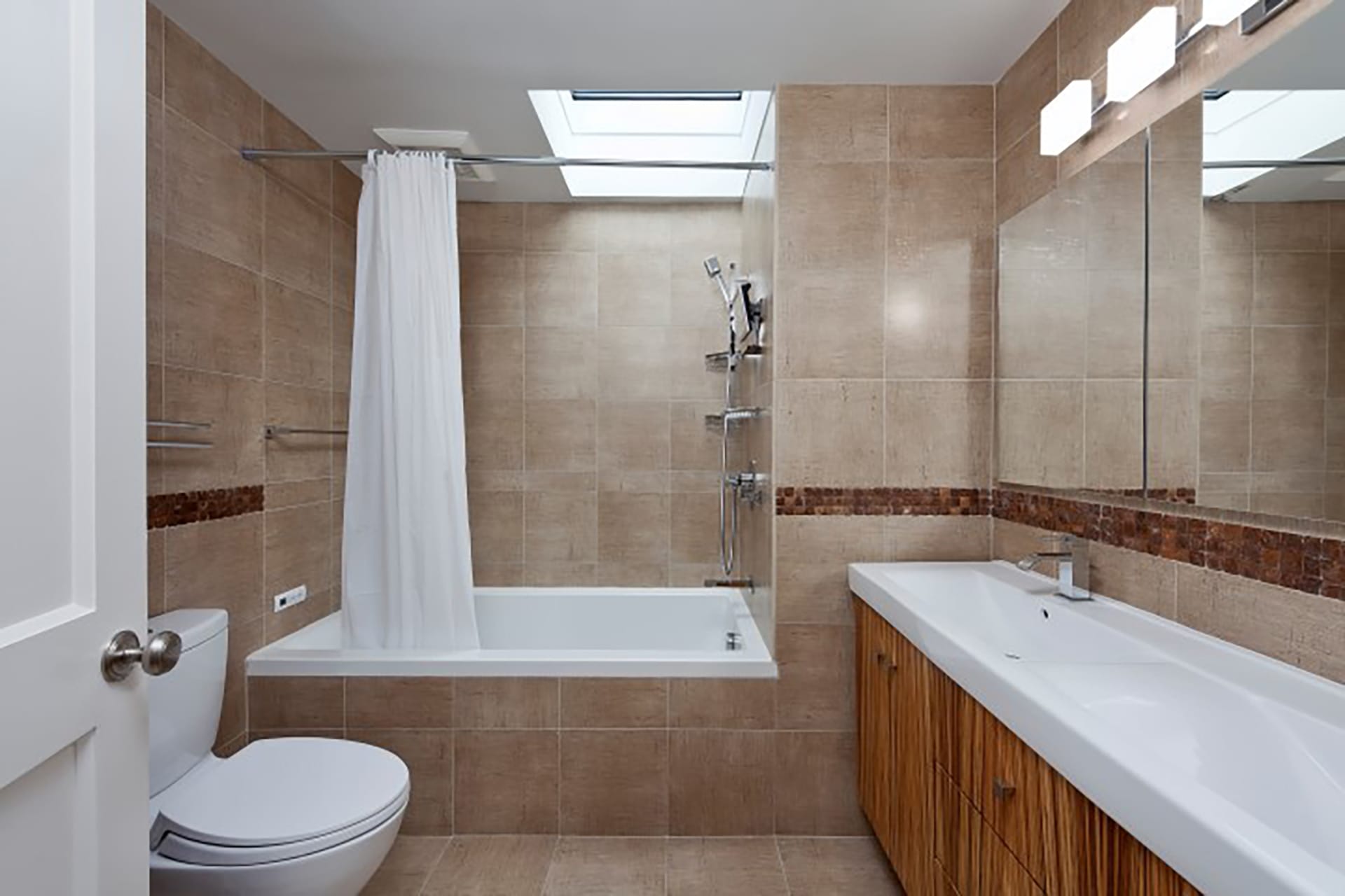 Primary bathroom with a skylight above the built-in tub, stone tiled walls and floors, and wood vanity