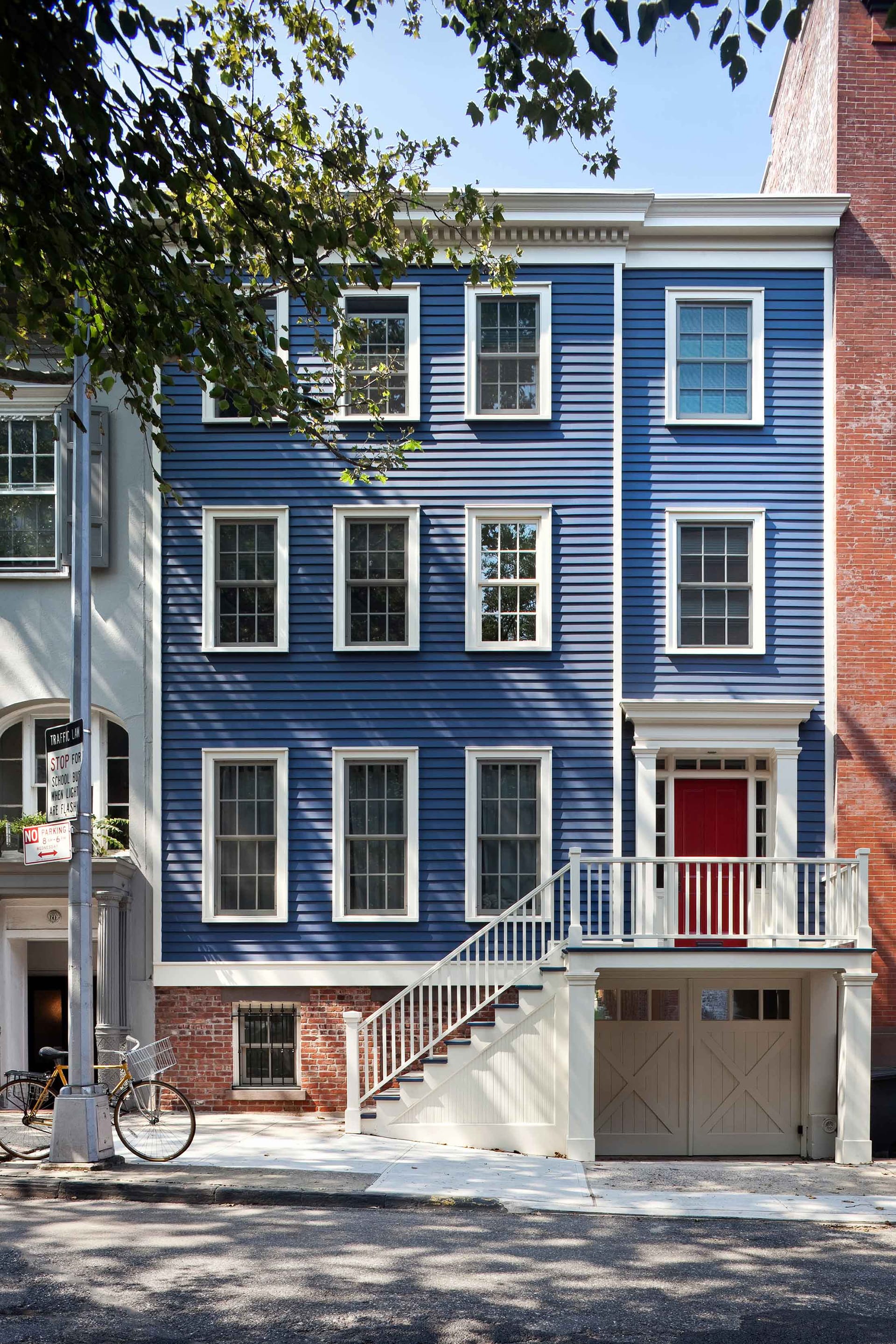 Restored front façade of a large rowhome with garden-level garage, blue siding, white trim, and a red front door.