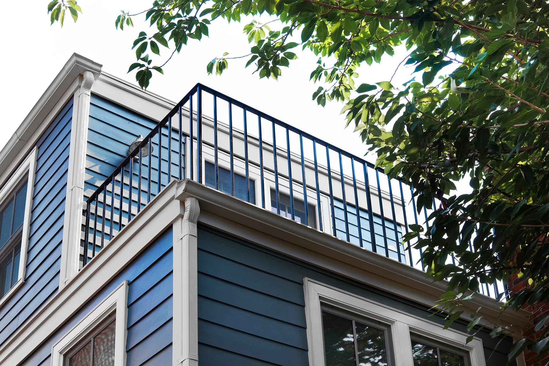 Rear upper-level balcony of a house clad with blue siding and white trim