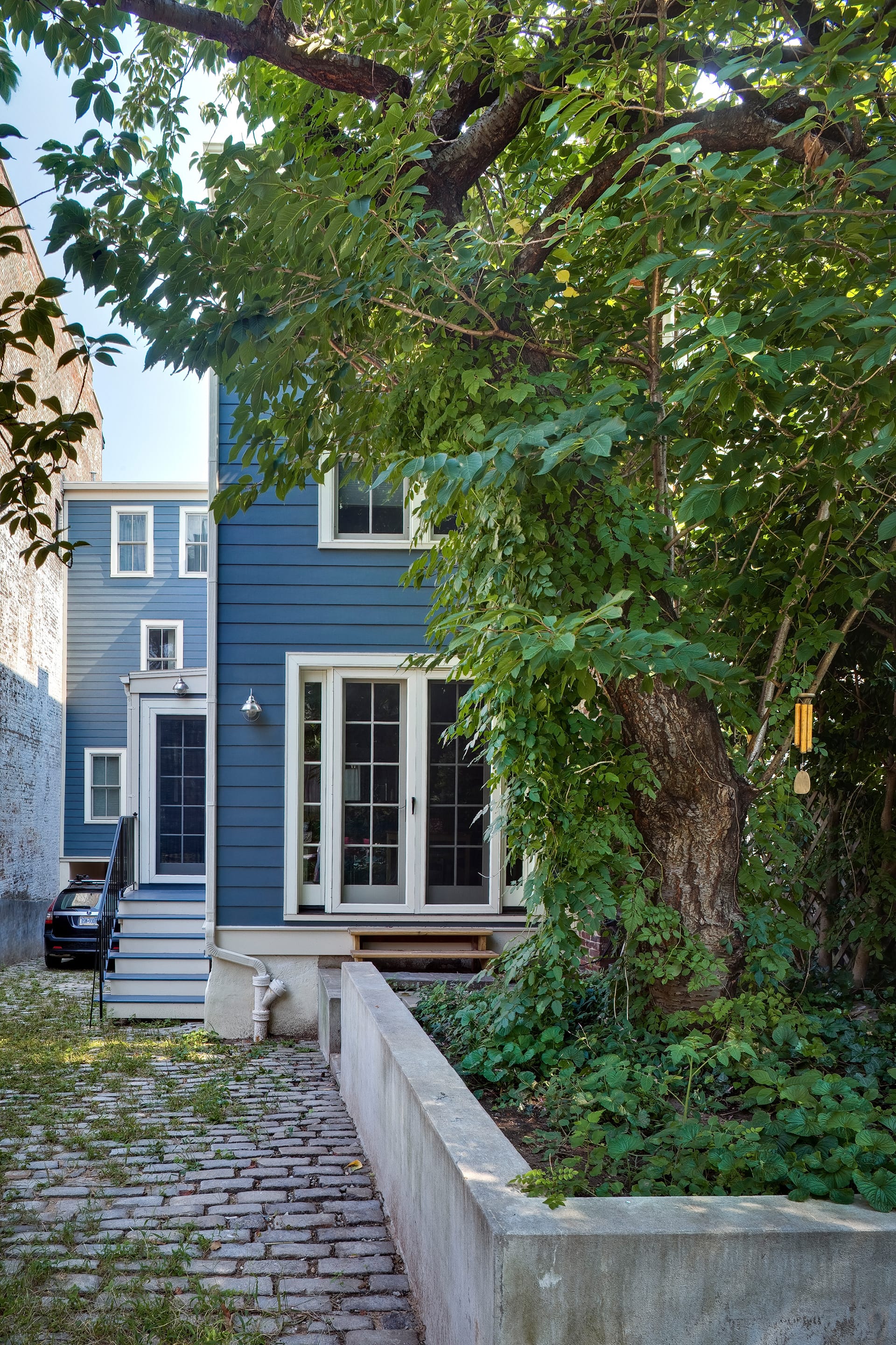 Rear façade of a home with blue siding, white trim, and brick paved driveway