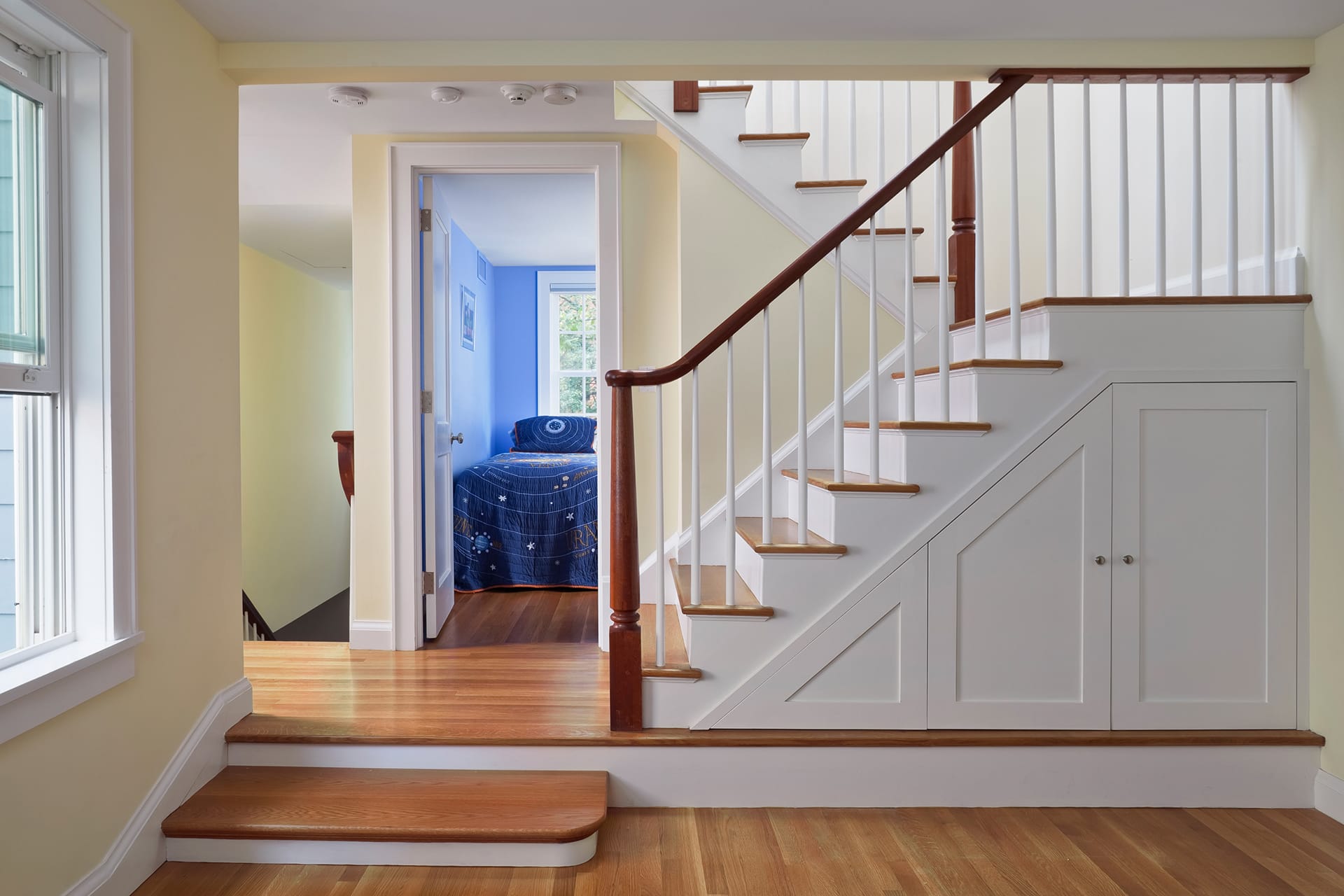 Stairwell with white millwork, dark wood floors and handrails, looking into a blue child's bedroom