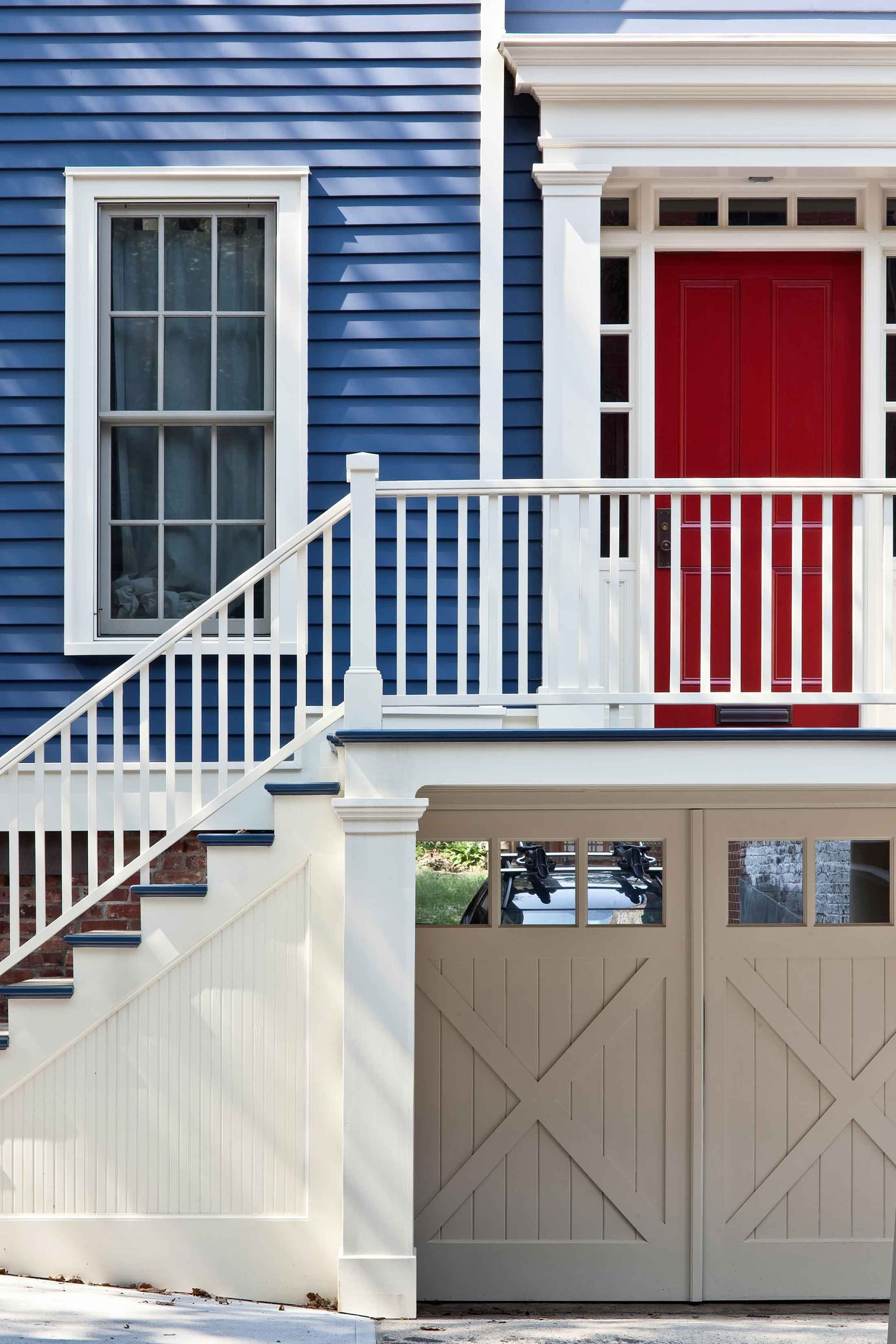 Restored front façade of a large rowhome with garden-level garage, blue siding, white trim, and a red front door.