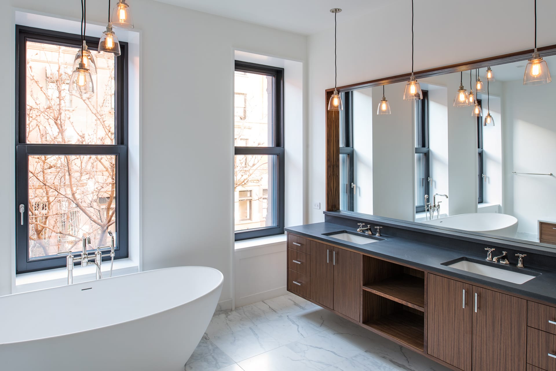 Freestanding tub, solid wood Jack and Jill vanity, and pendant lights in the primary bathroom of an Upper West Side Passive House.