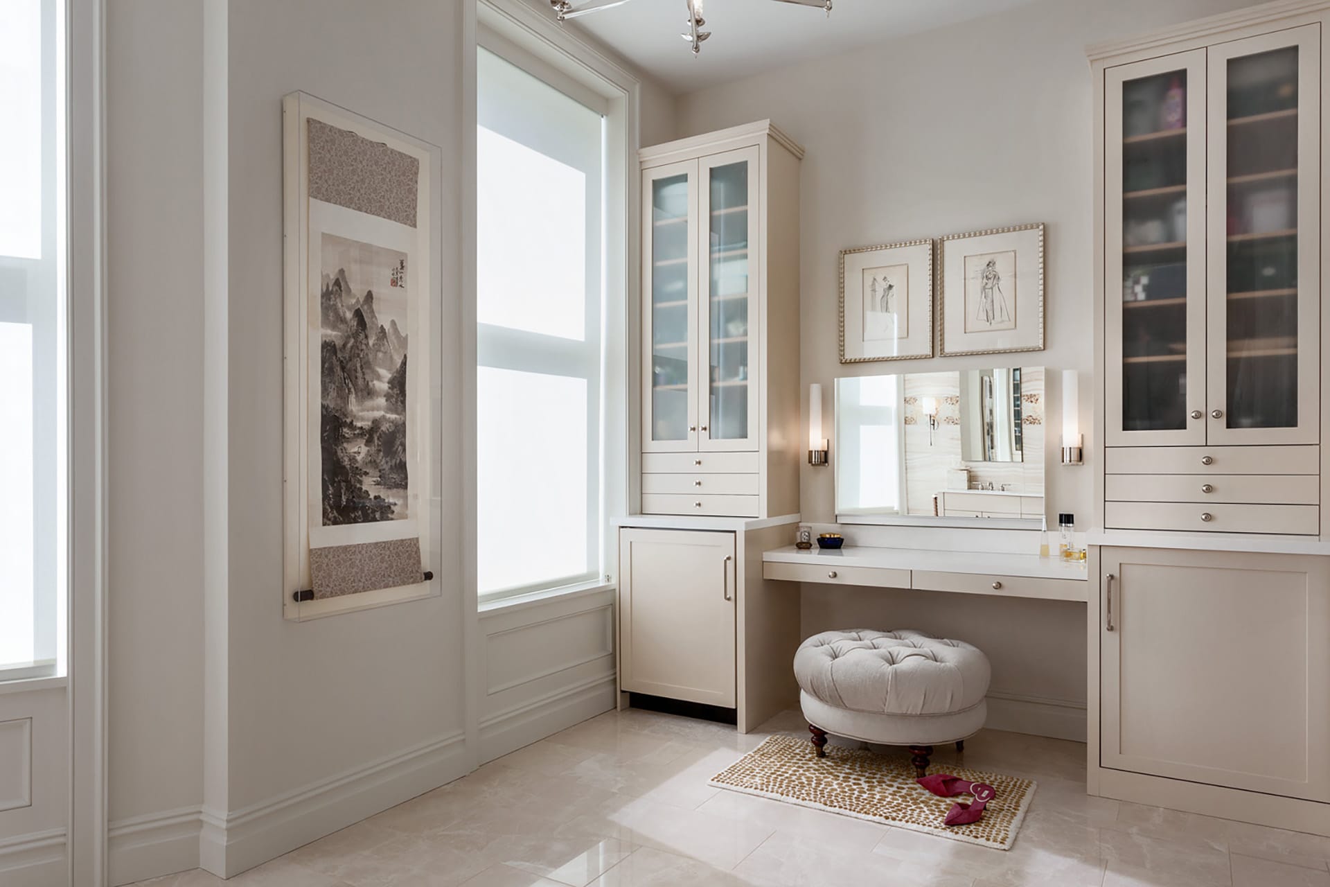 Off-white dressing area in a primary bathroom with custom vanities next to a large window