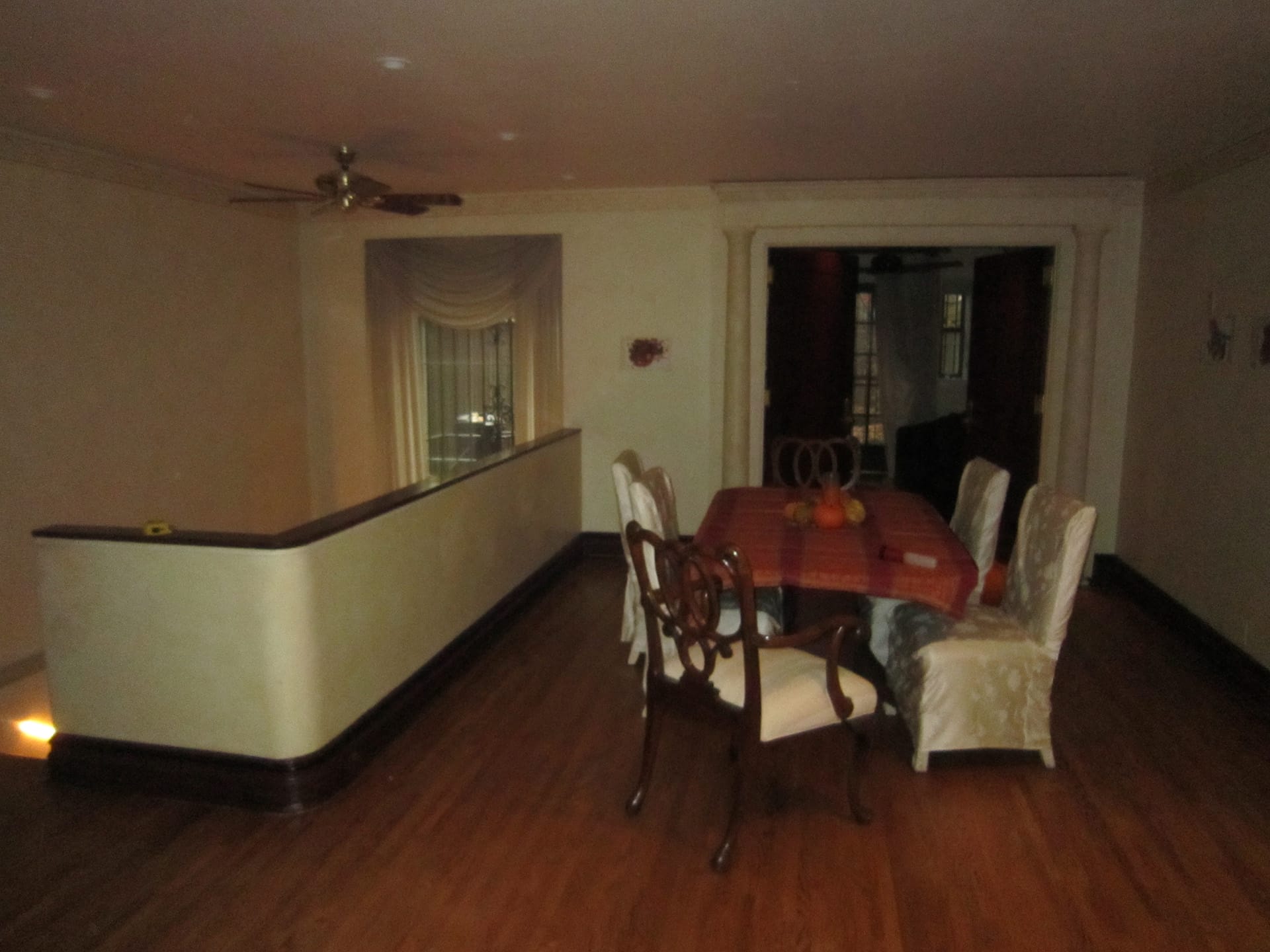 Dining room with mismatched chairs, dark wood floors, and a ceiling fan before our renovation
