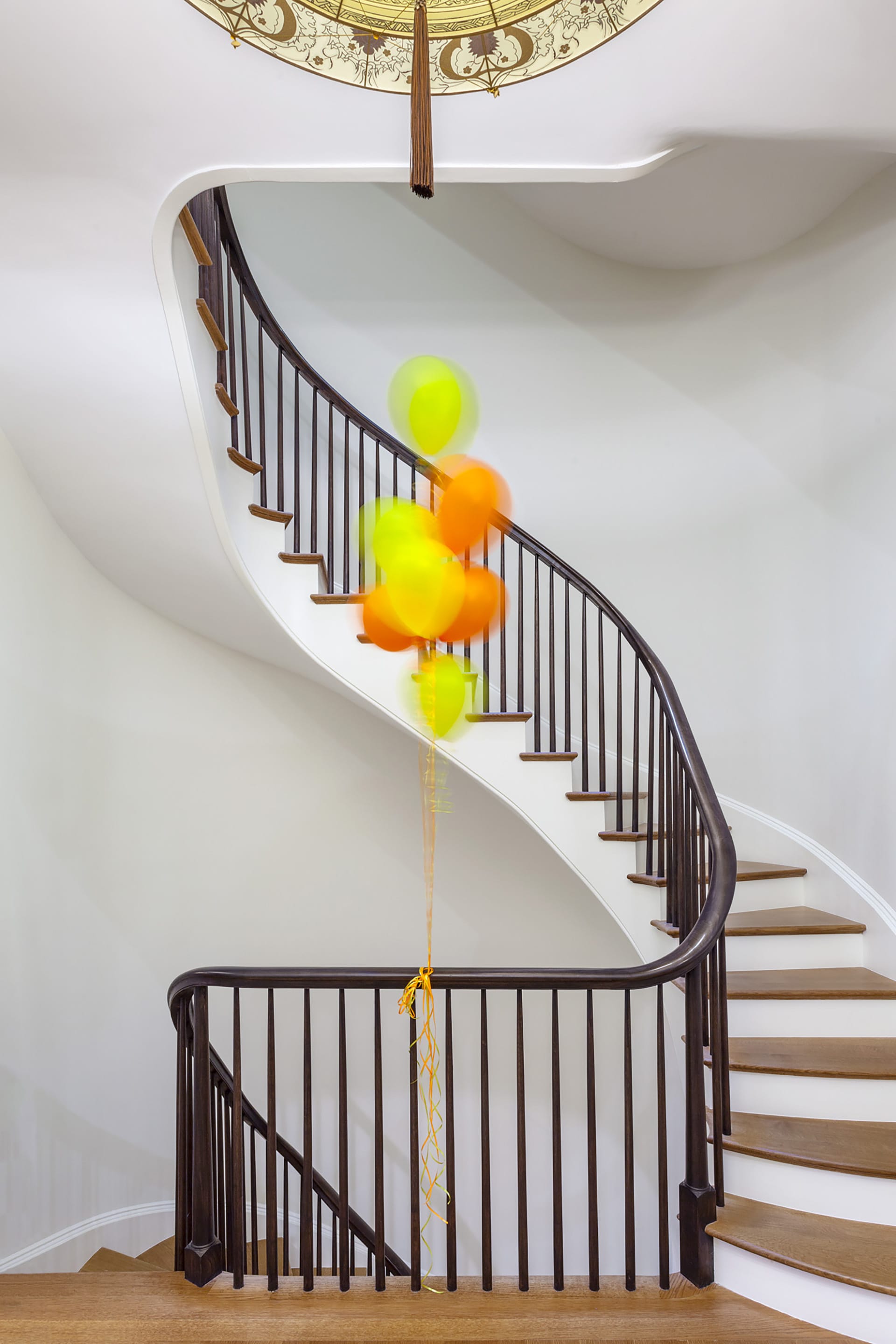 Sculptural staircase with an antique chandelier and a group of balloons ascending the space in the middle.
