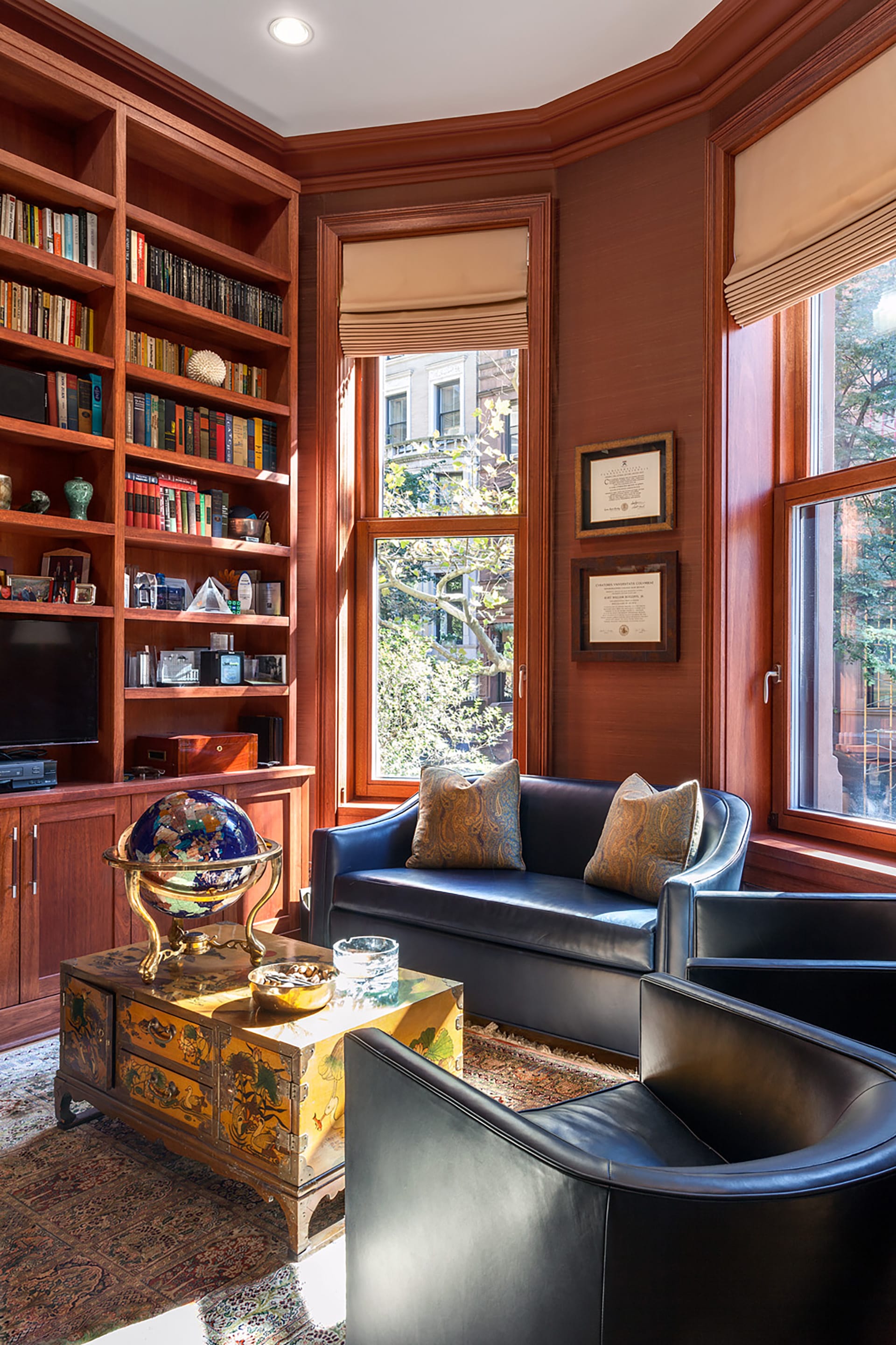 Wood-paneled study with roman shades and built-in bookshelves at the front of an Upper West Side townhouse.