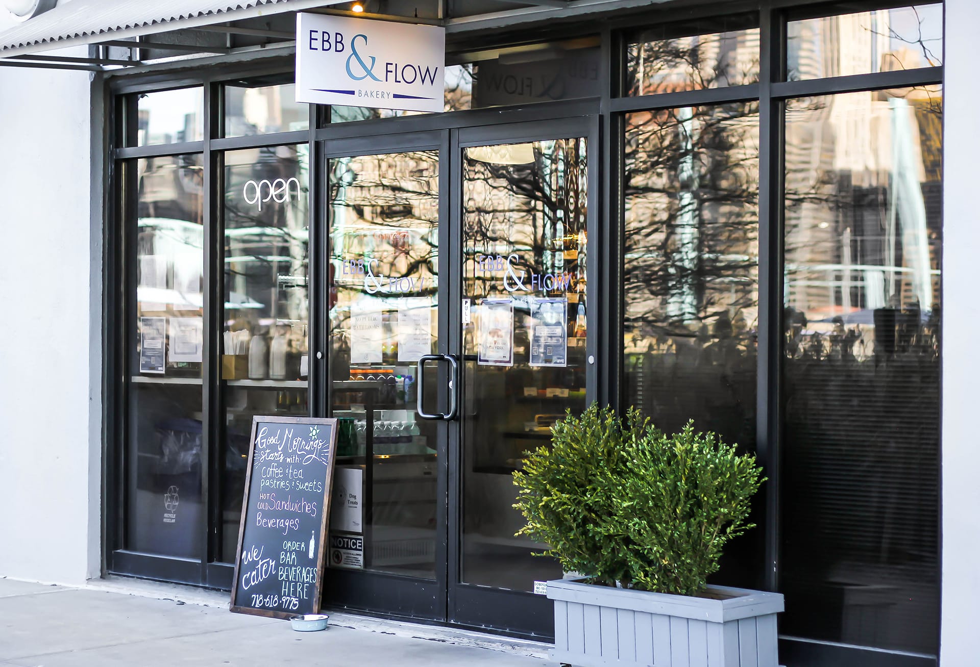 Glass storefront of the Ebb & Flow Bakery with a sign hanging above the door and a chalkboard sign next to the front doors.