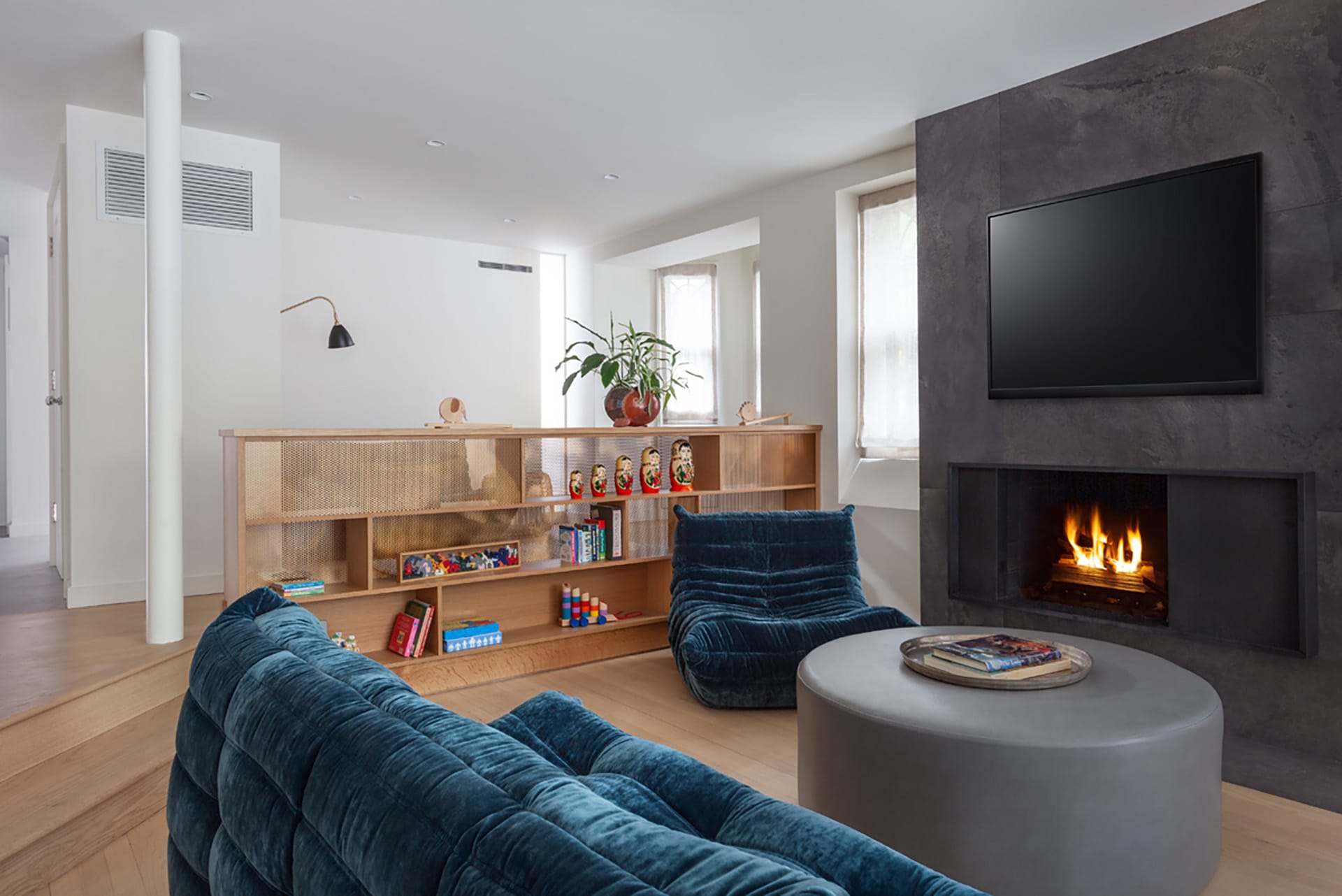 Garden level entryway and entertainment space in a Park Slope room with a large grey fireplace and blue velvet seating