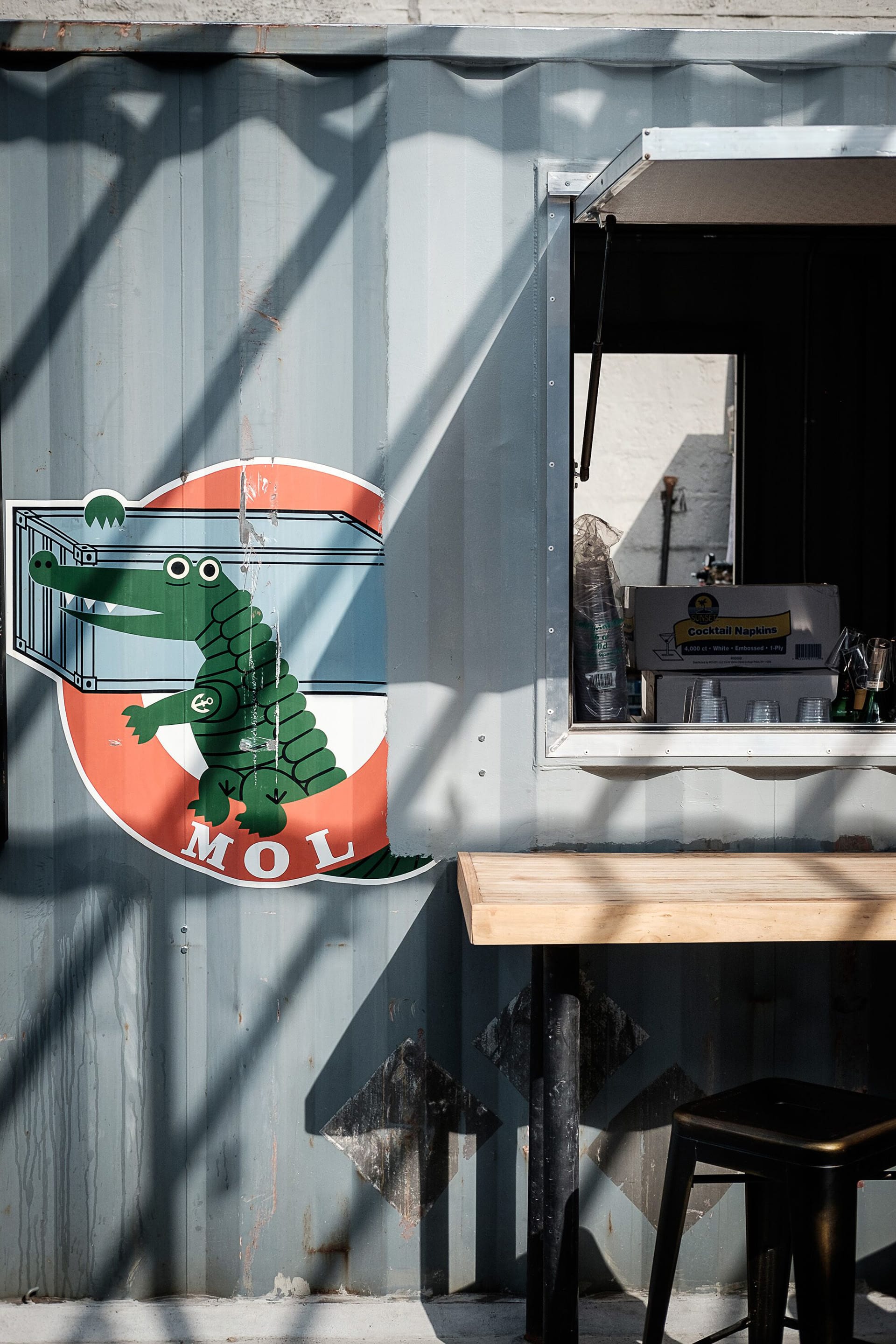 Pickup window at a taco stand with a wood bar in front and an alligator painted on the wall.