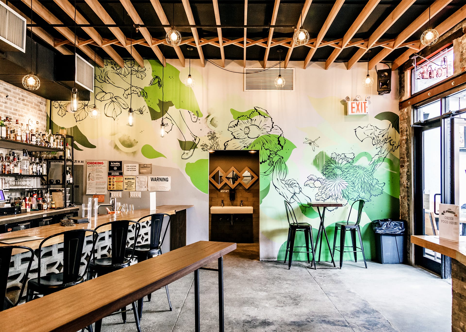 Interior of Parklife, with exposed beams on the ceiling, concrete floors, a green floral mural on the wall, and a bar to the left of the image.