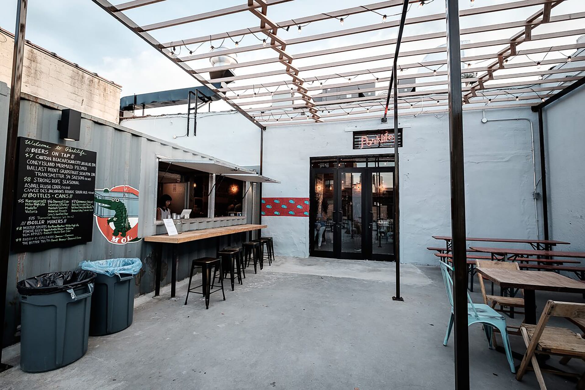 Entrance to Parklife with a pergola, grey walls, picnic tables, and a window where guests can purchase tacos.