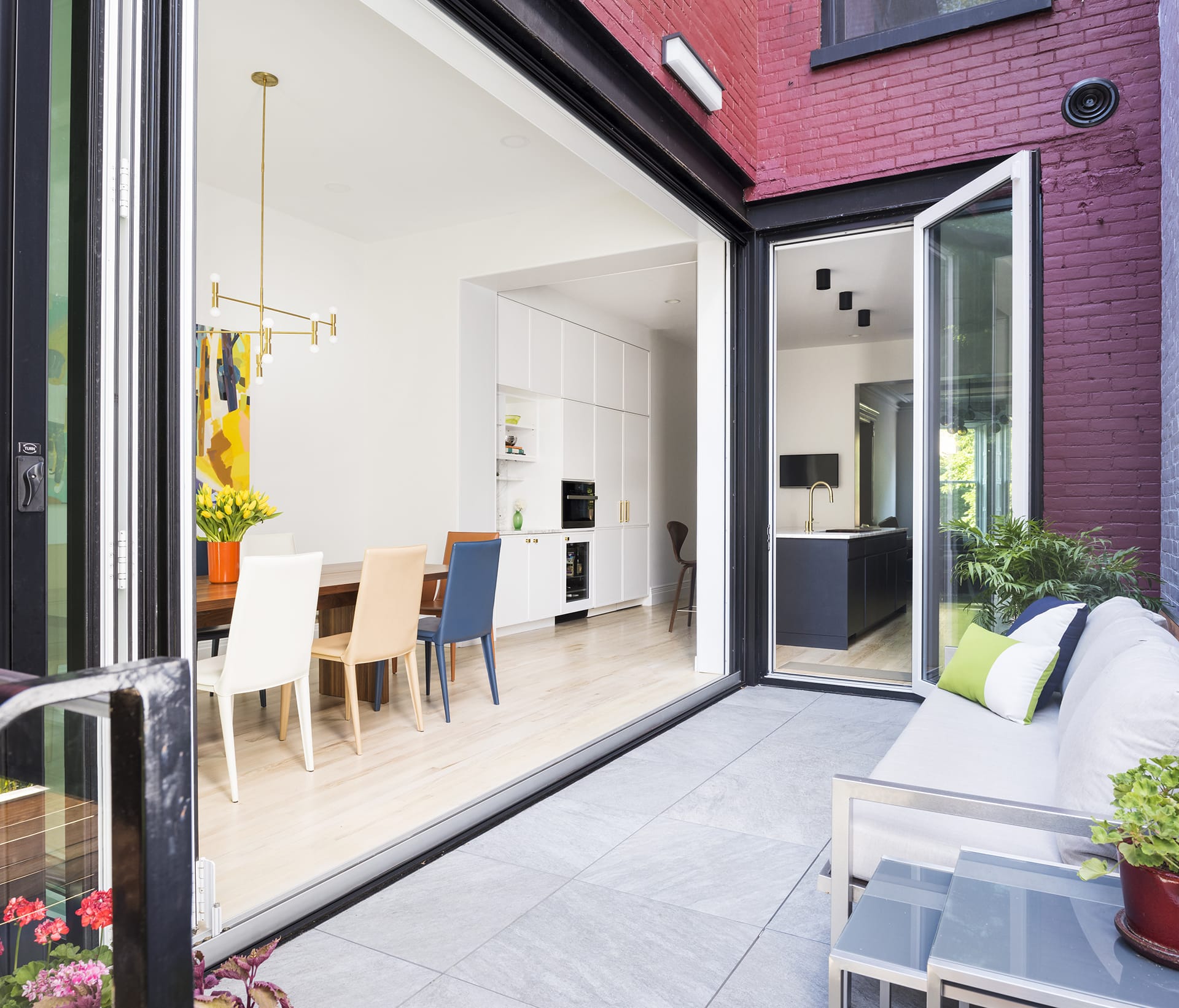 Rear façade of a red-painted brick townhouse with a large NanaWall open to the dining room and kitchen