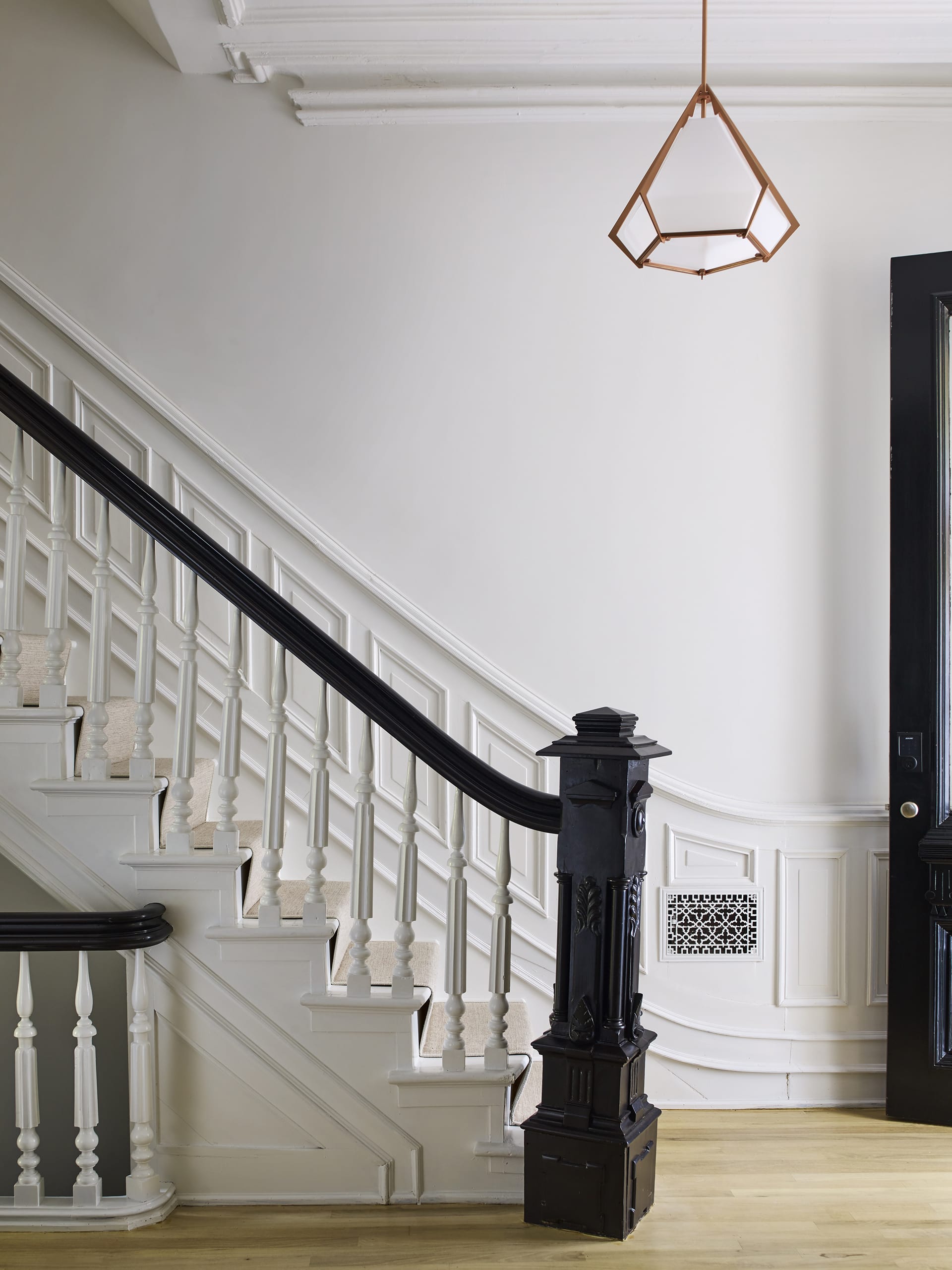 Entryway of a Prospect Heights home with a pendant light and staircase with black newel post and railings and white posts.